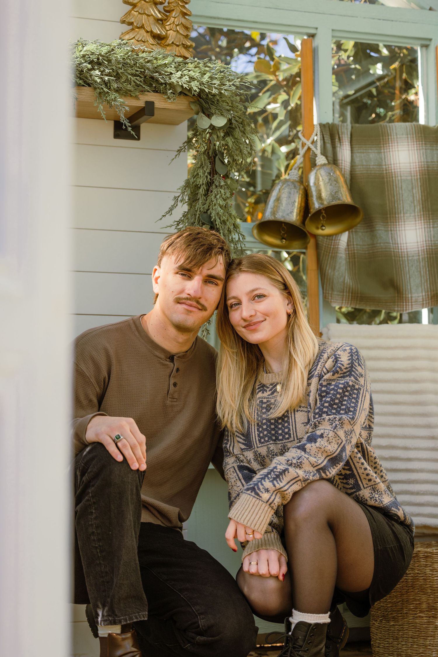 Couple sitting together outdoors during autumn with festive holiday decorations and greenery overhead. Christmas minis at lemon drop studios