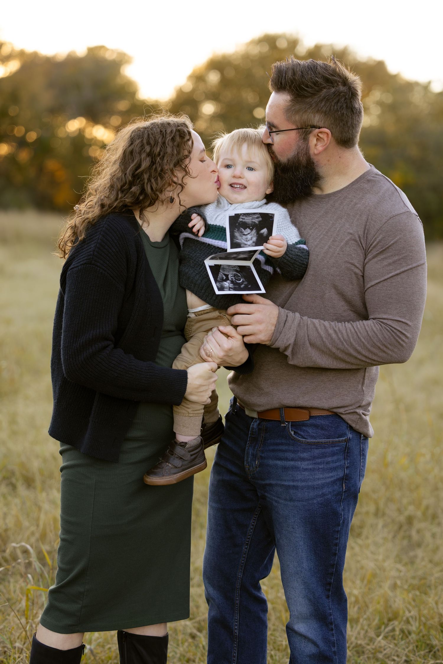 Family sharing joyful moment while holding ultrasound photo in golden sunset field. Pregnancy announcement photoshoot in forth worth, Keller