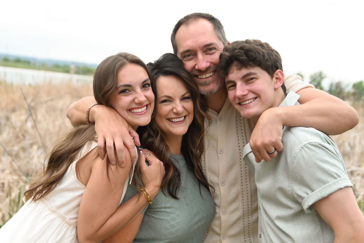 A happy family of four people embracing and smiling together outdoors on a sunny day.