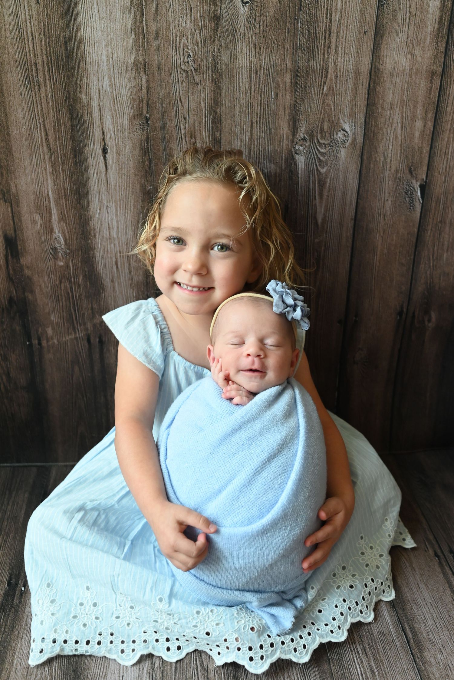 Two siblings in matching light blue outfits pose together against a rustic wooden backdrop.