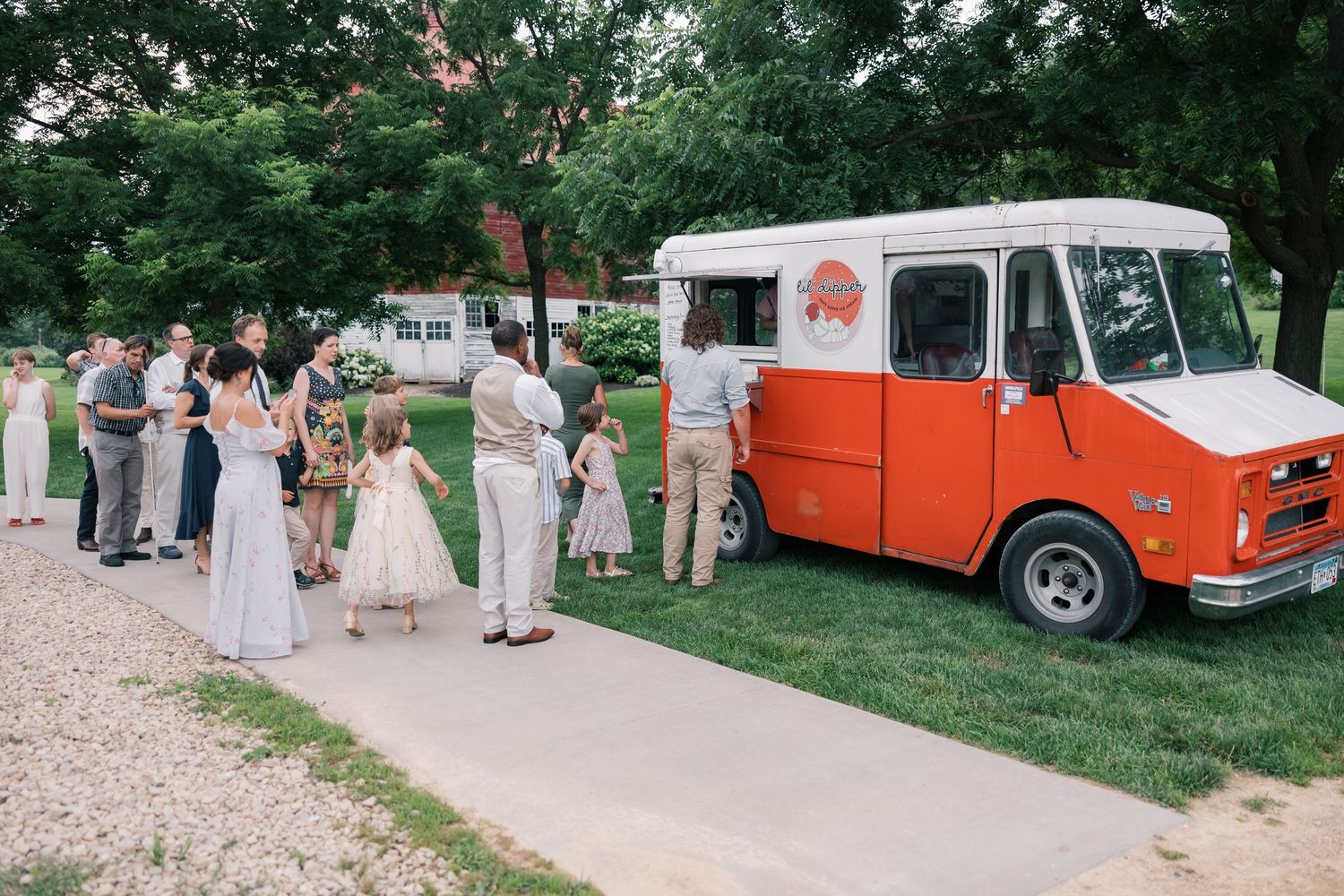 Vintage orange food truck parked at an outdoor wedding reception with guests nearby.