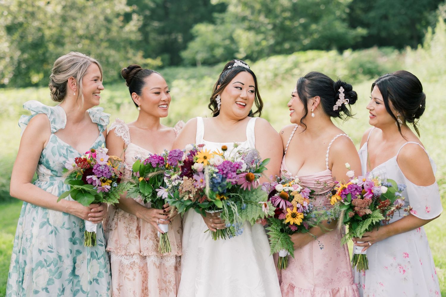 Bridesmaids in floral dresses holding colorful bouquets outdoors.