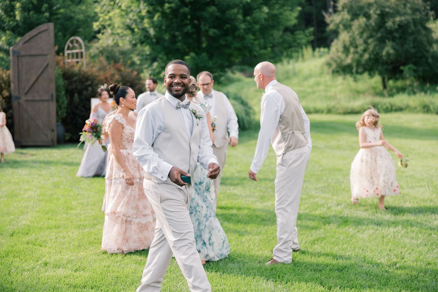Wedding party in pastel attire walks together across sunny green lawn.