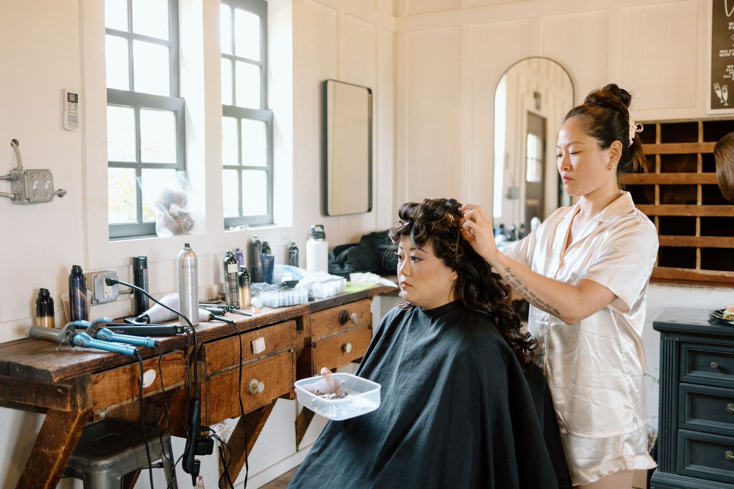 Professional barber working with client in a modern barbershop with bright windows and vintage decor.
