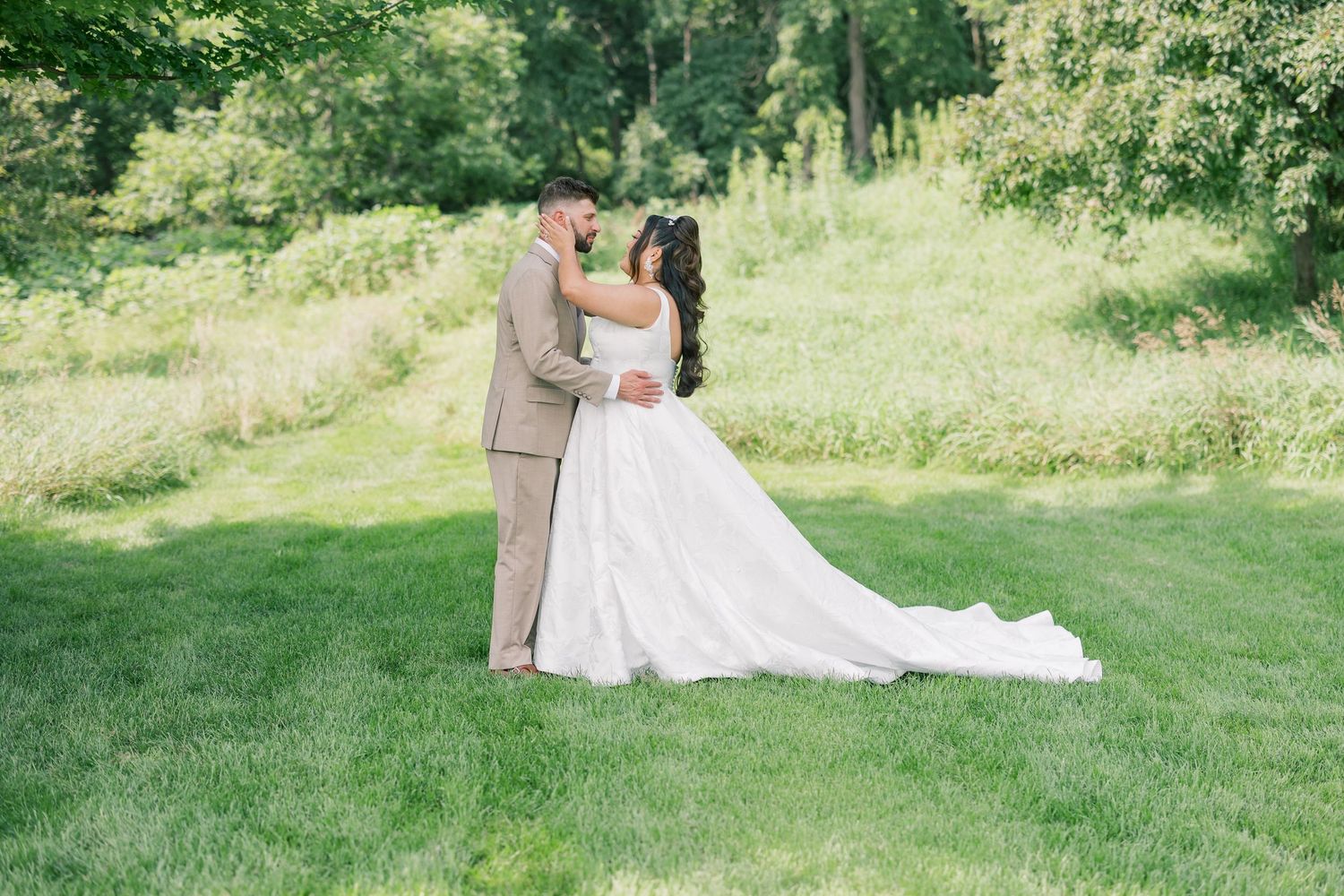 Wedding couple poses together on a scenic grassy hillside surrounded by greenery.