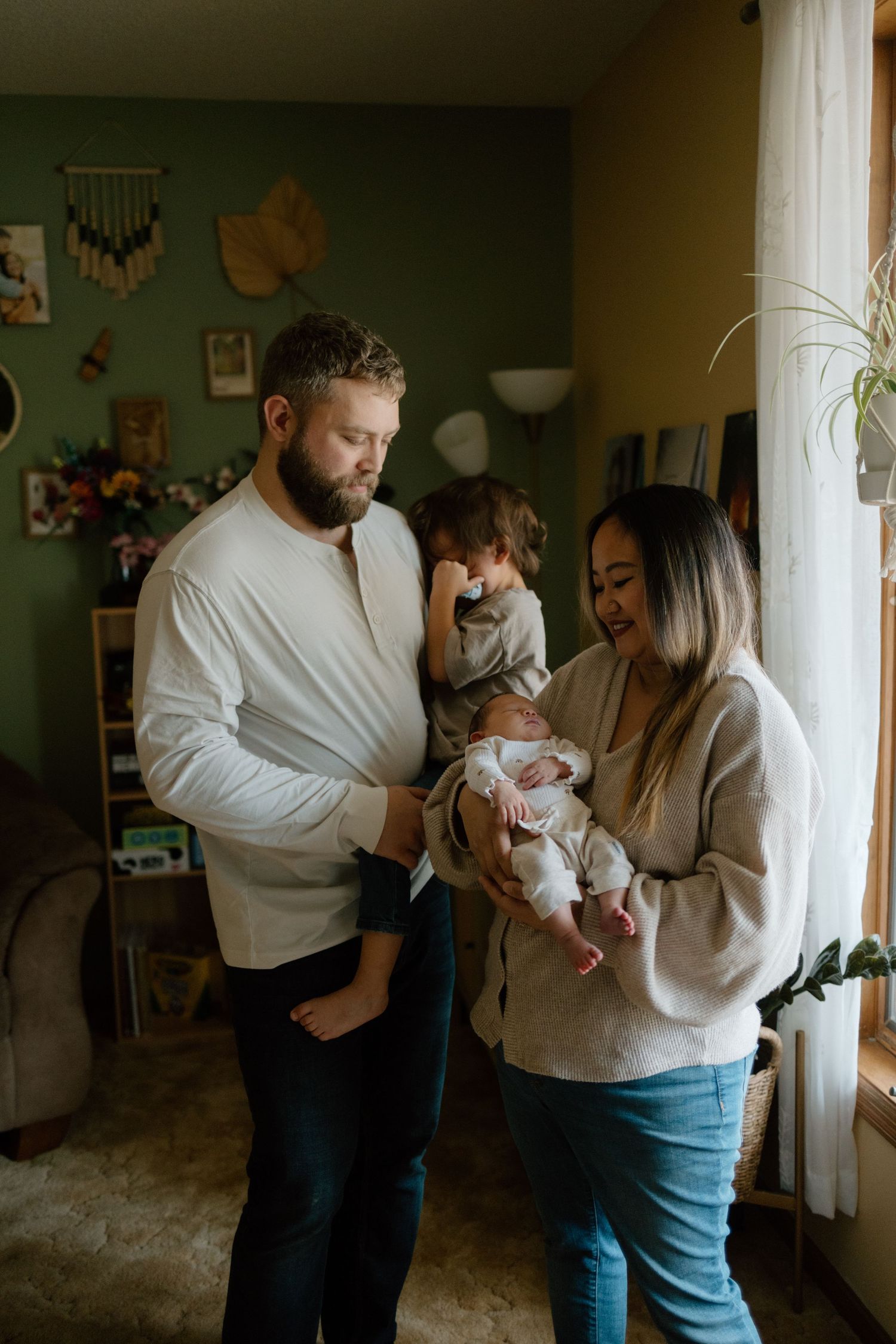 A couple in a living room shares tender moments while holding their newborn baby in a series of intimate photographs.