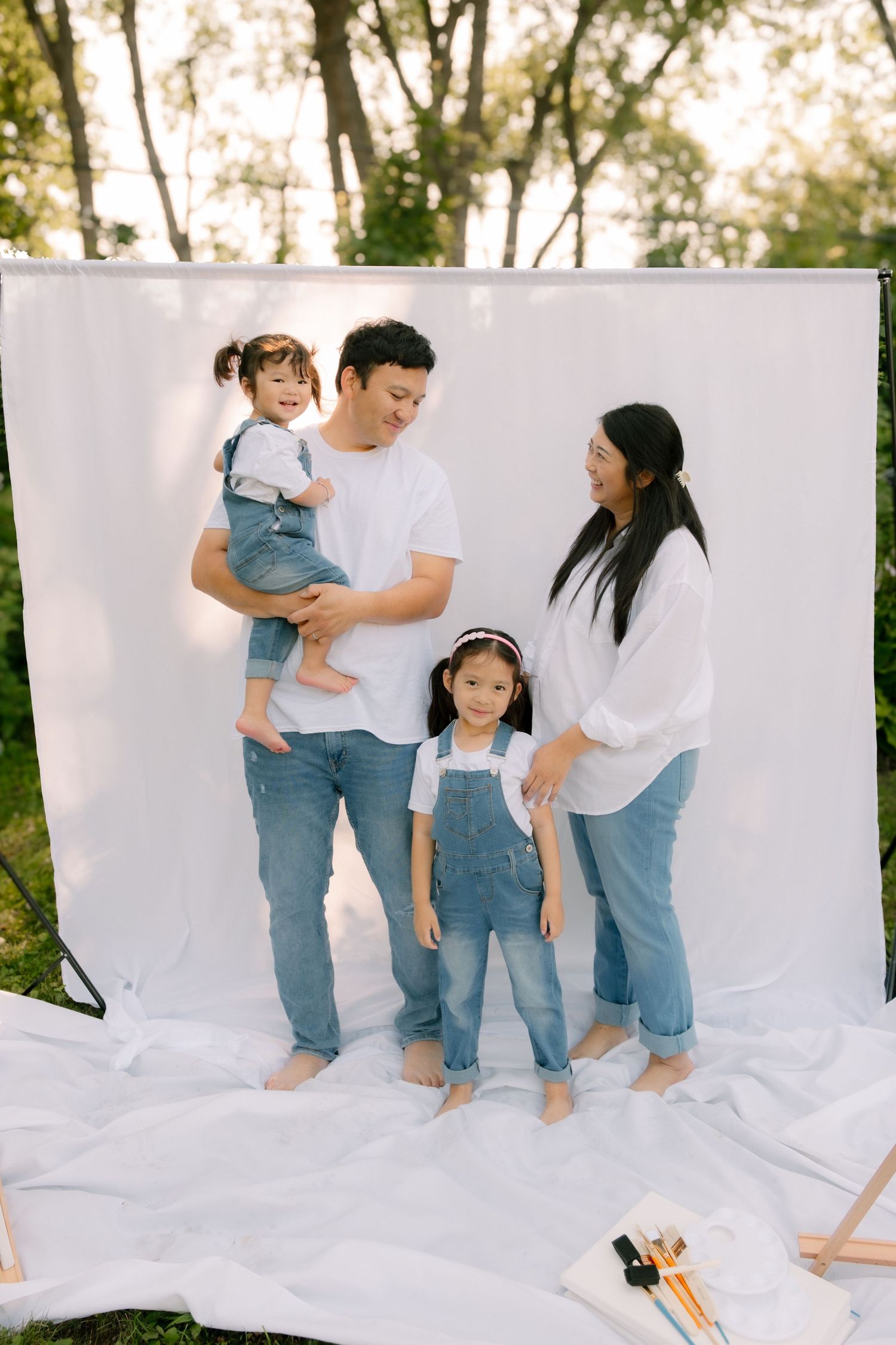 Happy Asian family of four poses together in front of a white backdrop outdoors.