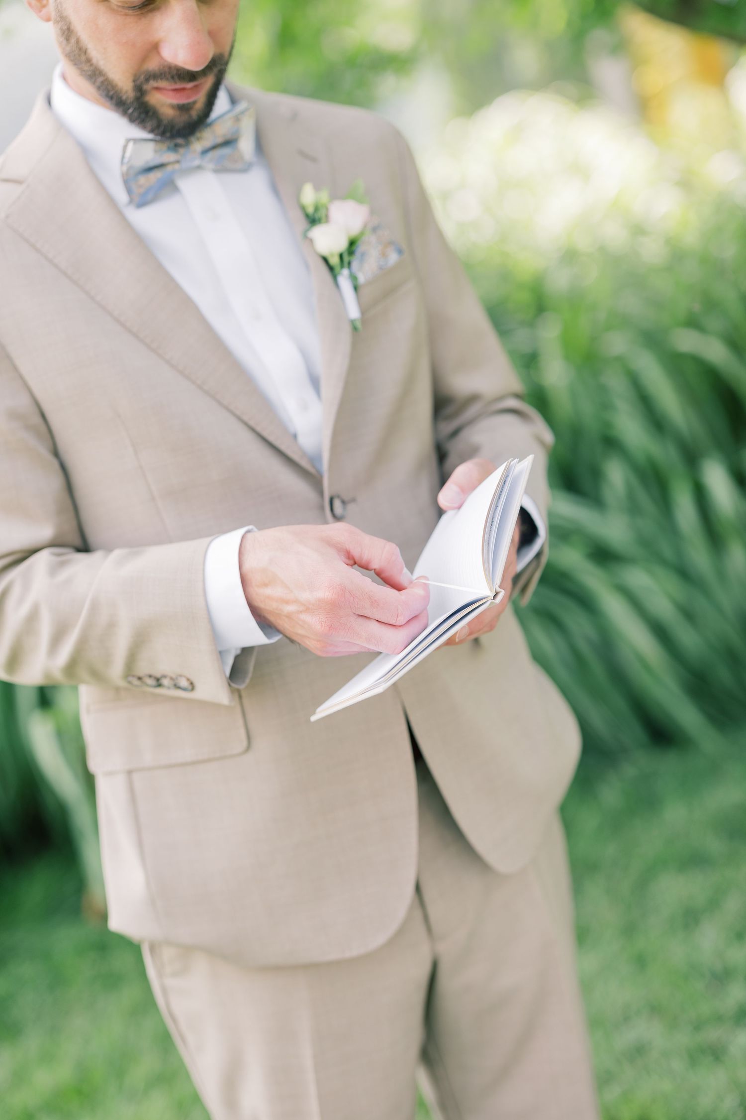Person in beige suit holding papers while standing outdoors against a green natural background.