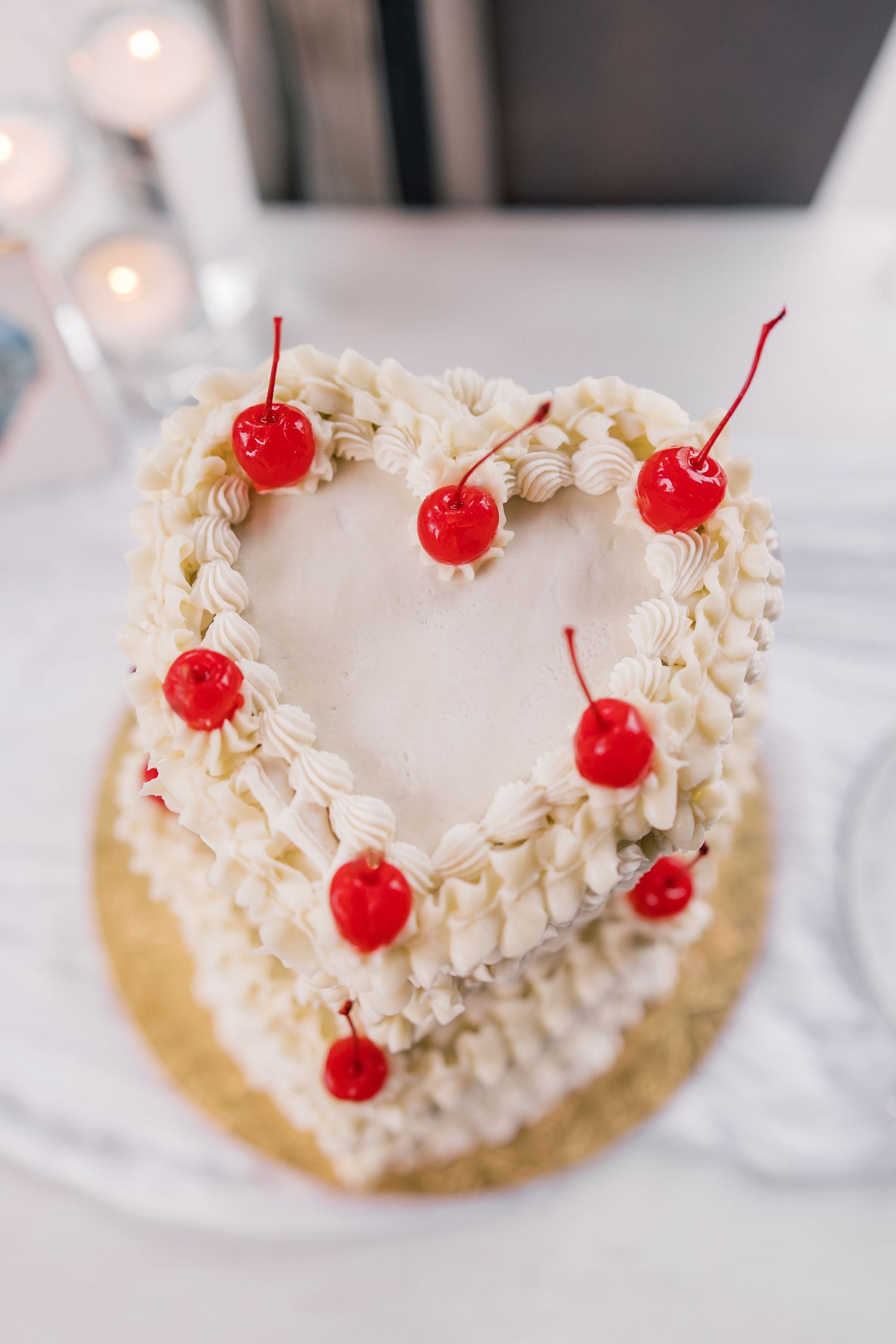 Heart-shaped white frosted cake topped with bright red maraschino cherries.
