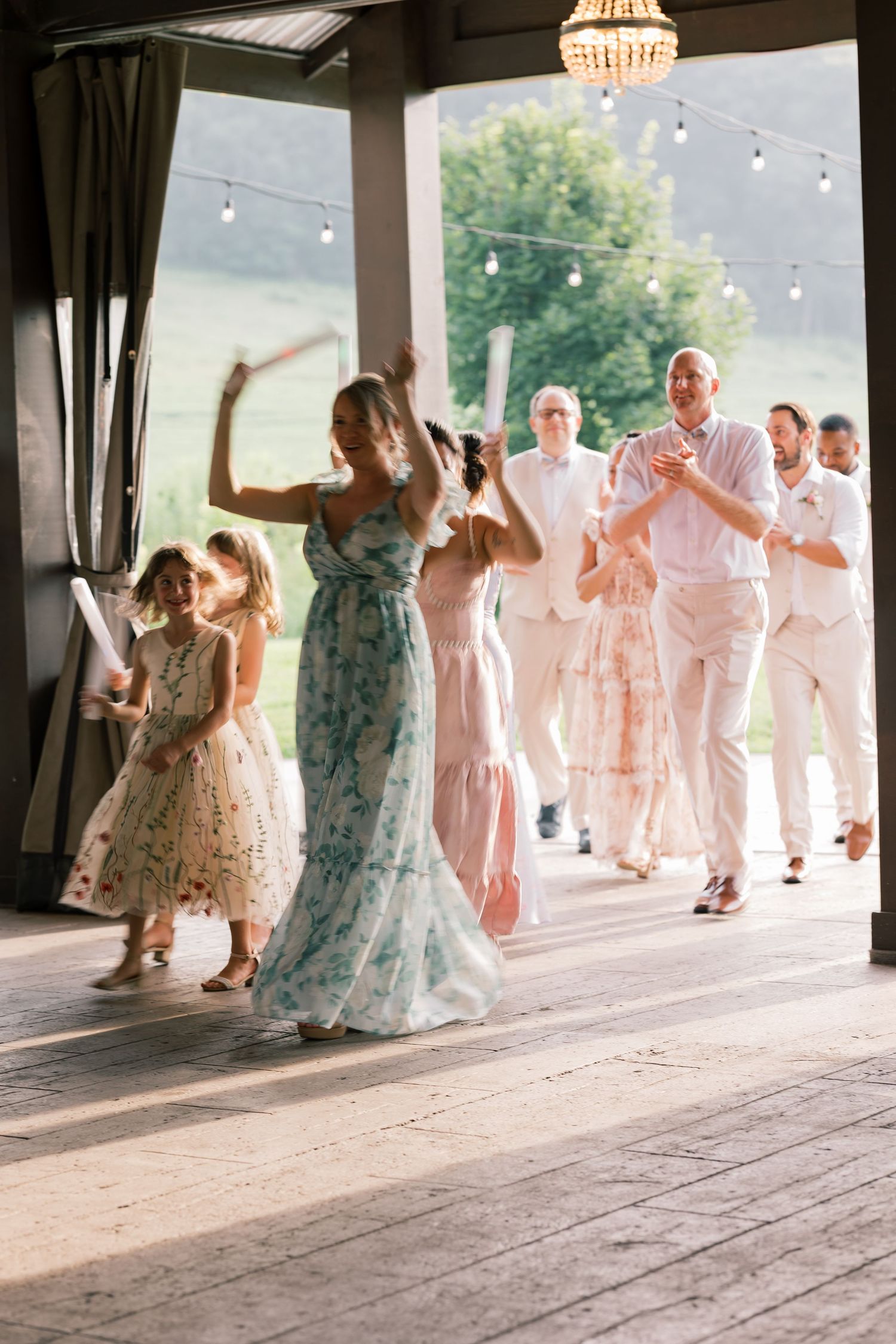 Wedding guests dance together in formal attire on a rustic wooden dance floor at an outdoor covered venue.