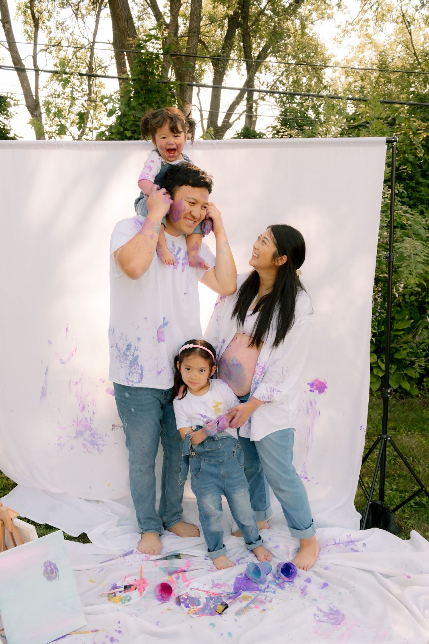 Happy family with two kids covered in purple paint posing outdoors in front of a white backdrop.