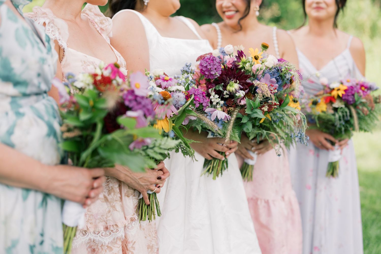 Vibrant wildflower bouquets held by wedding party members in pastel dresses.
