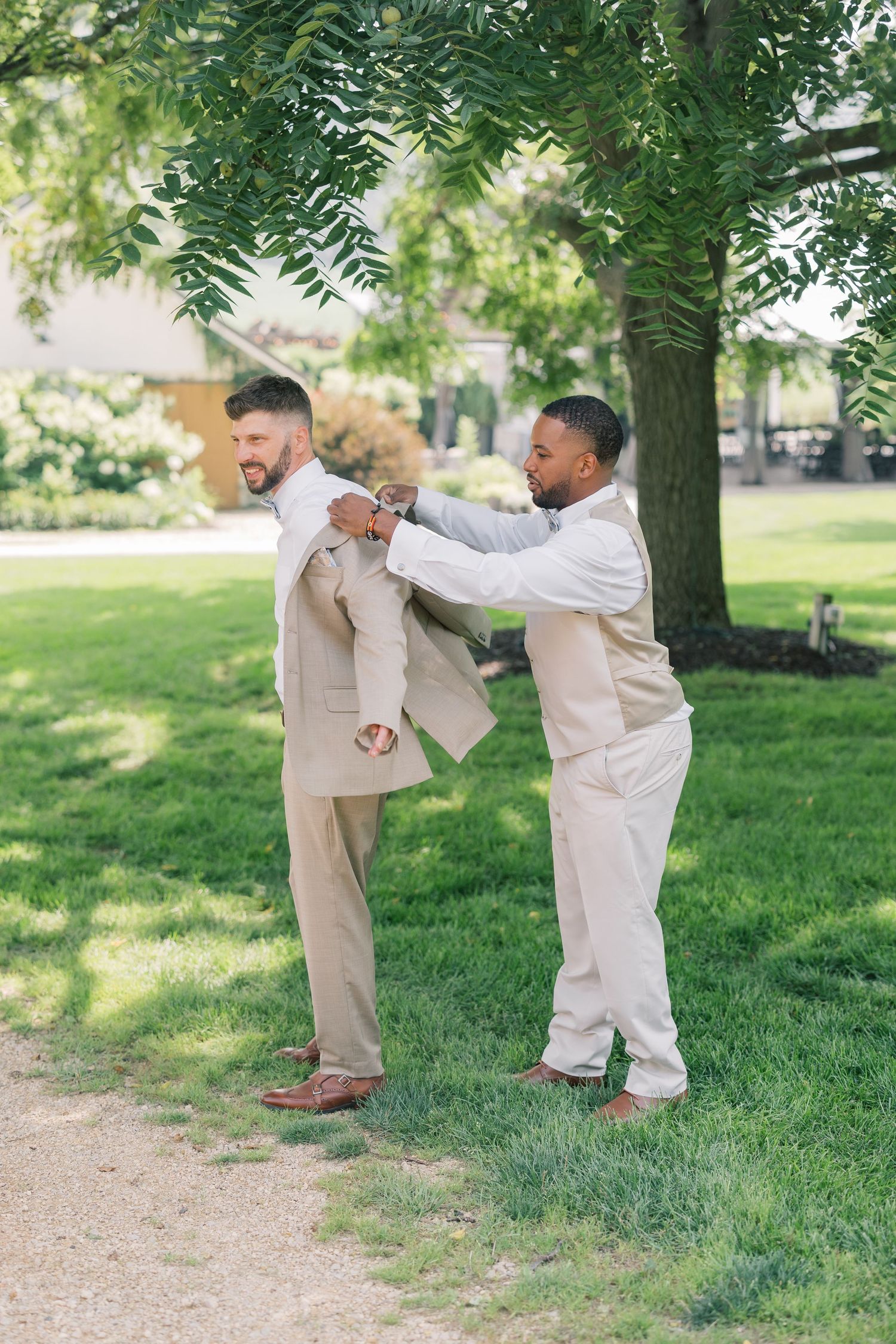 Young children in beige suits playing and running together on grass under trees.