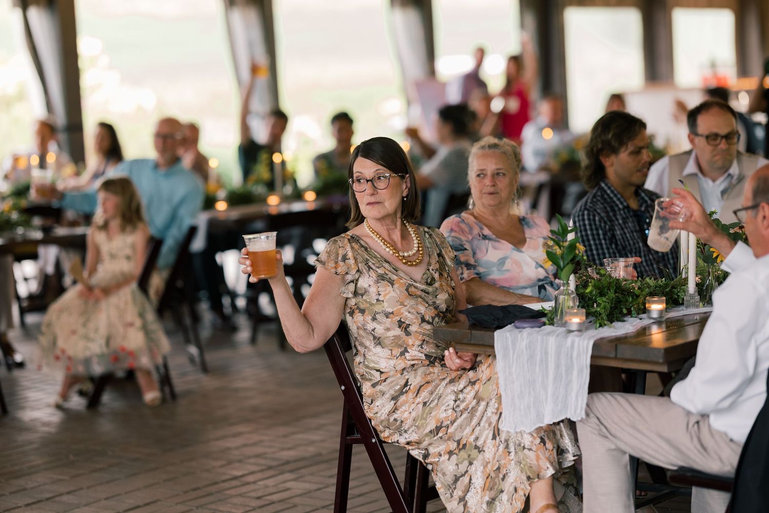 Wedding reception guests enjoying drinks and conversation under covered outdoor venue.