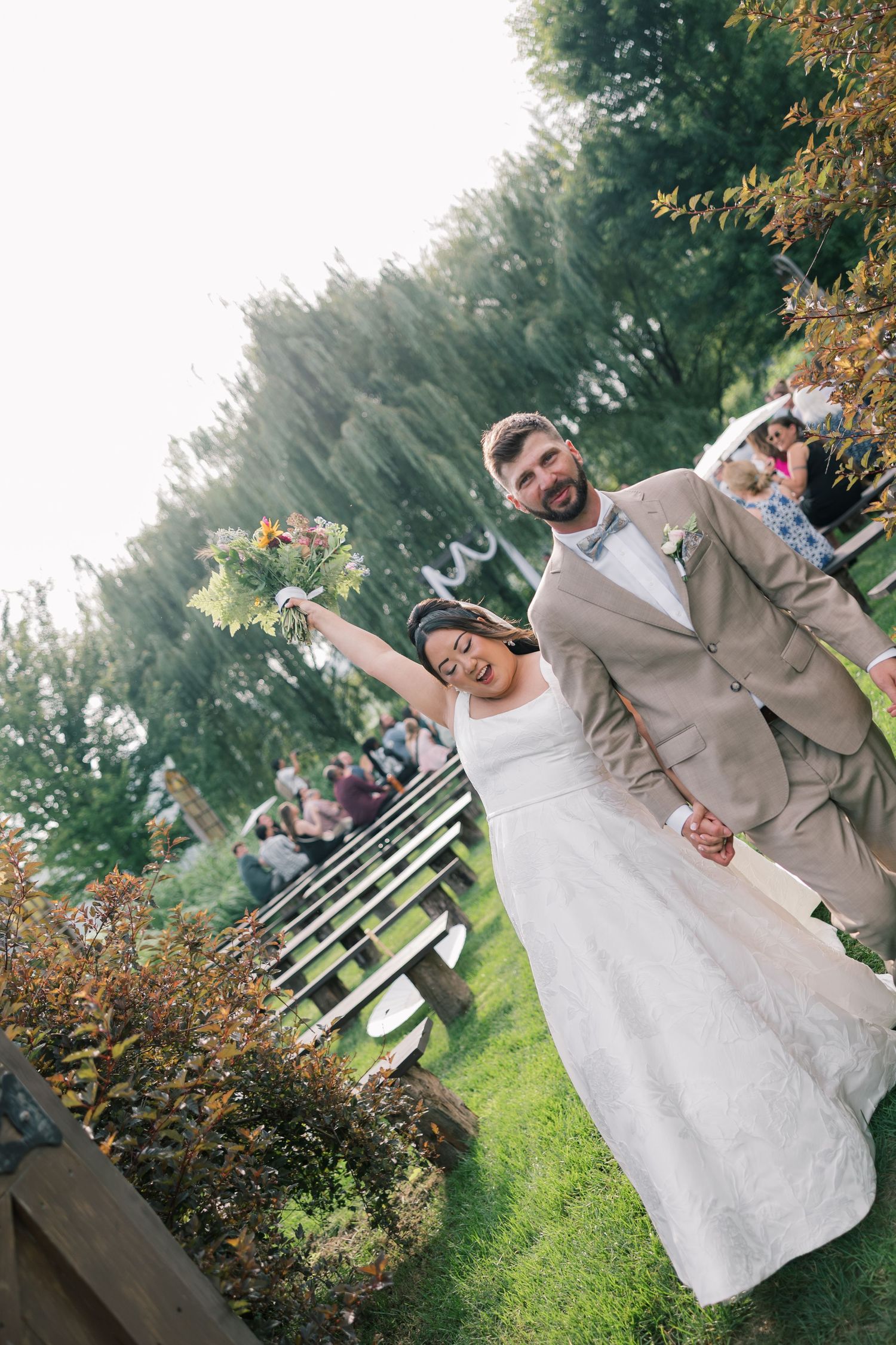 Newlyweds pose for candid photos in a garden setting with guests in background.