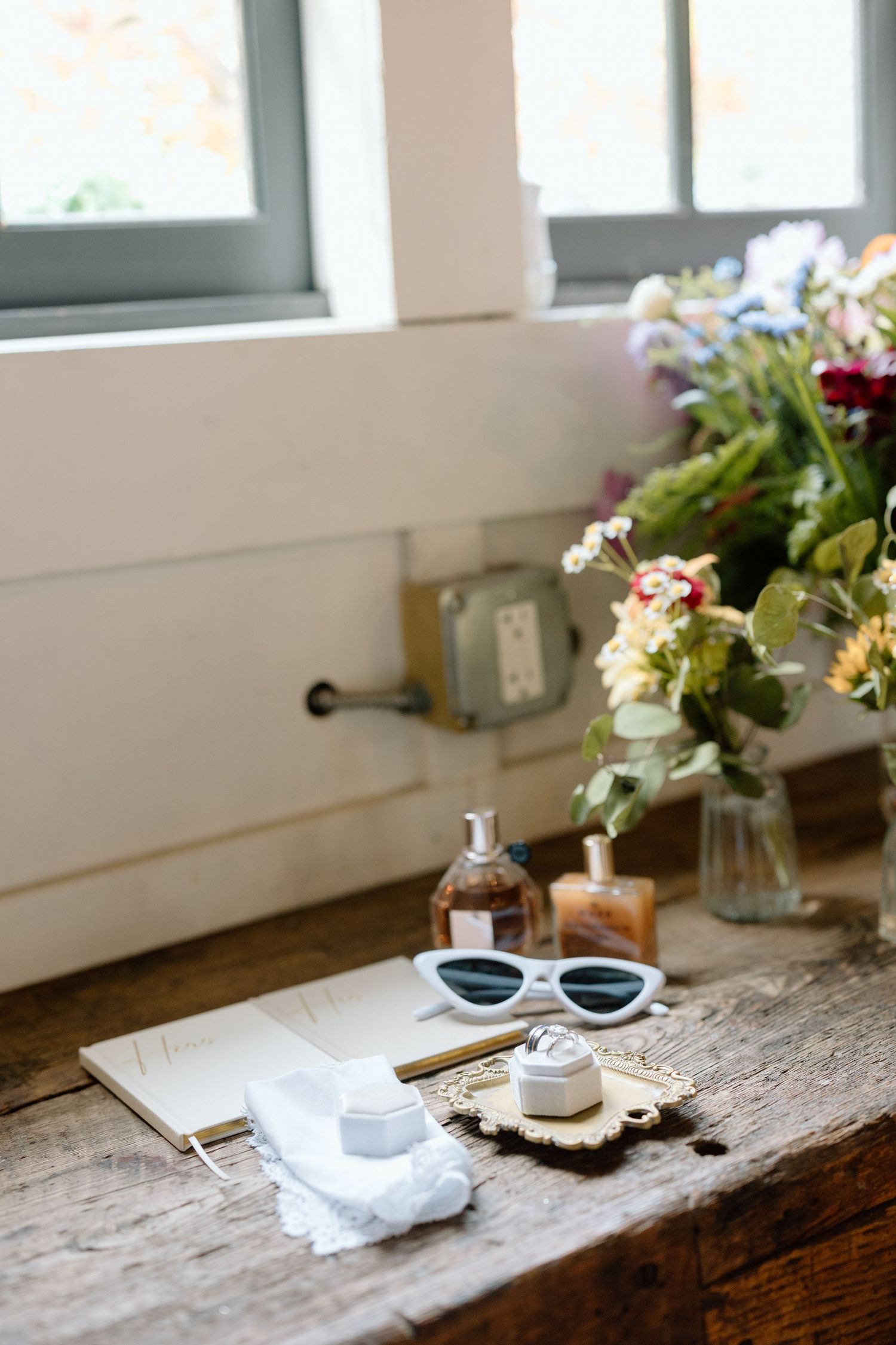 Wedding accessories including sunglasses and decor arranged on rustic wooden table near window.