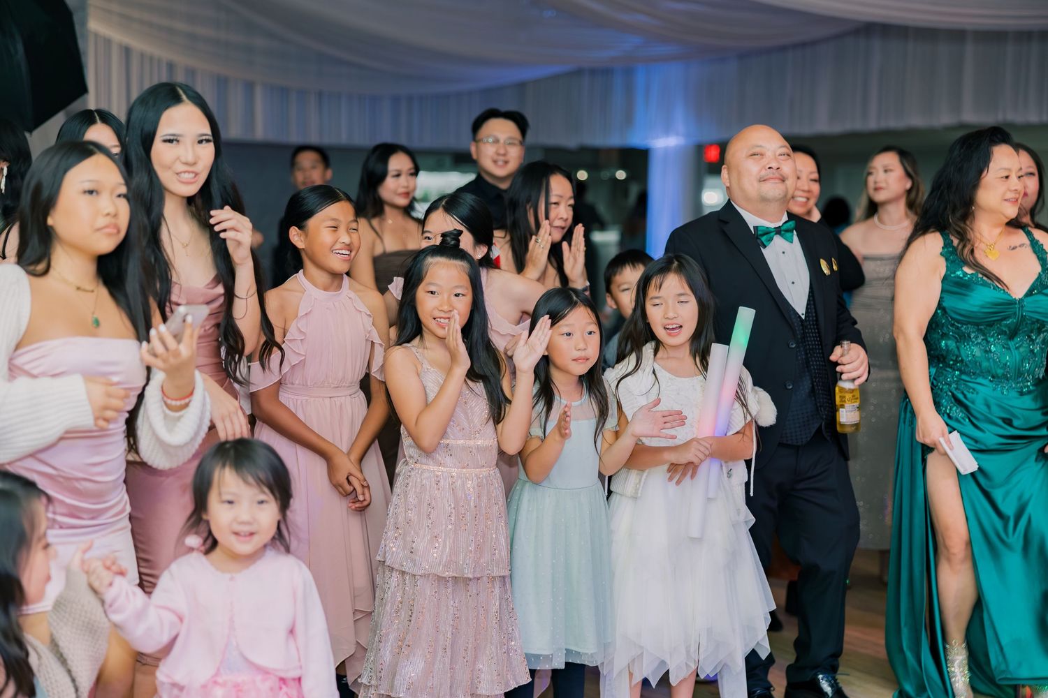 Wedding guests in pink and teal dresses dancing and celebrating on a reception dance floor.