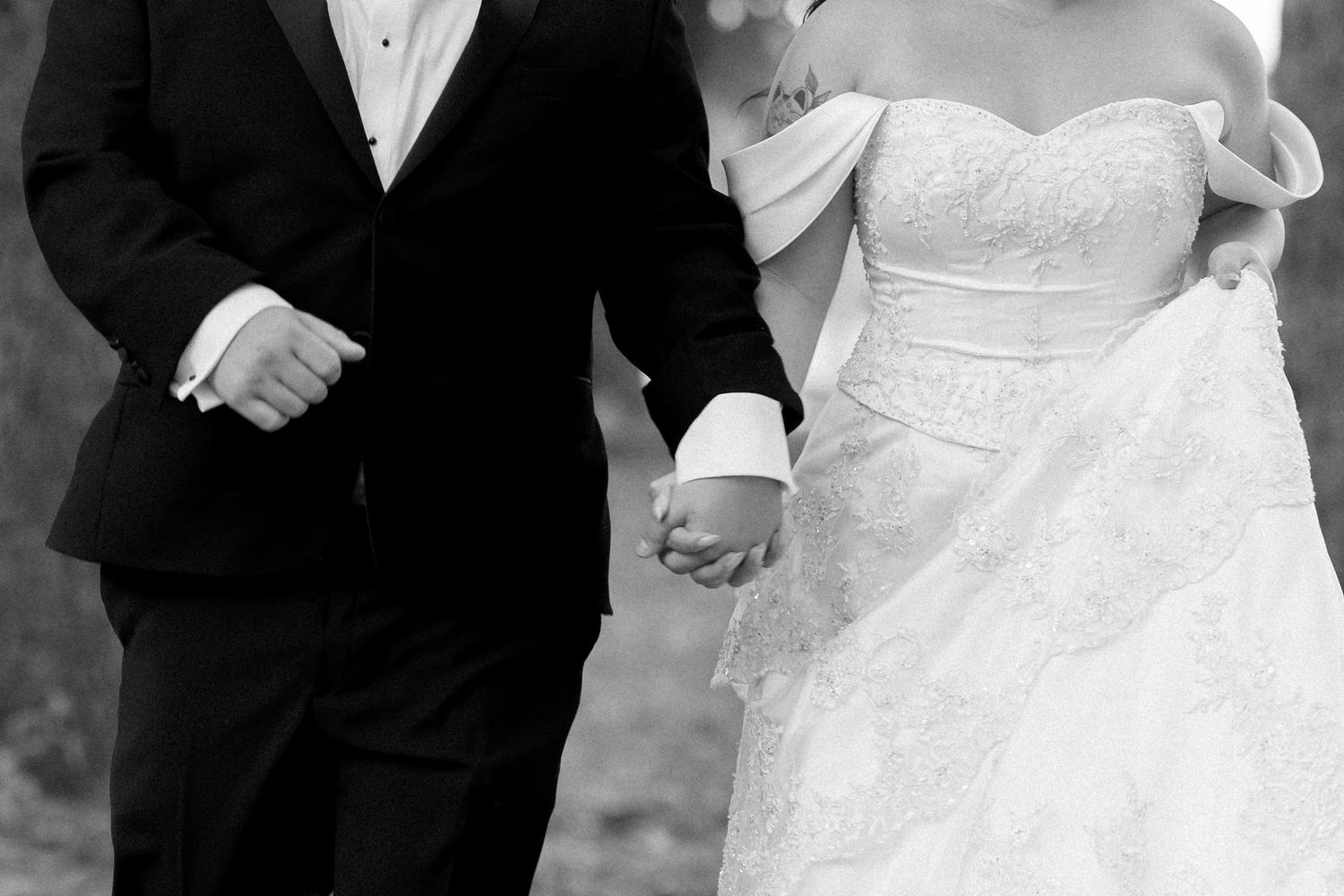 A wedding couple stands together in formal attire with their hands clasped during an outdoor ceremony.