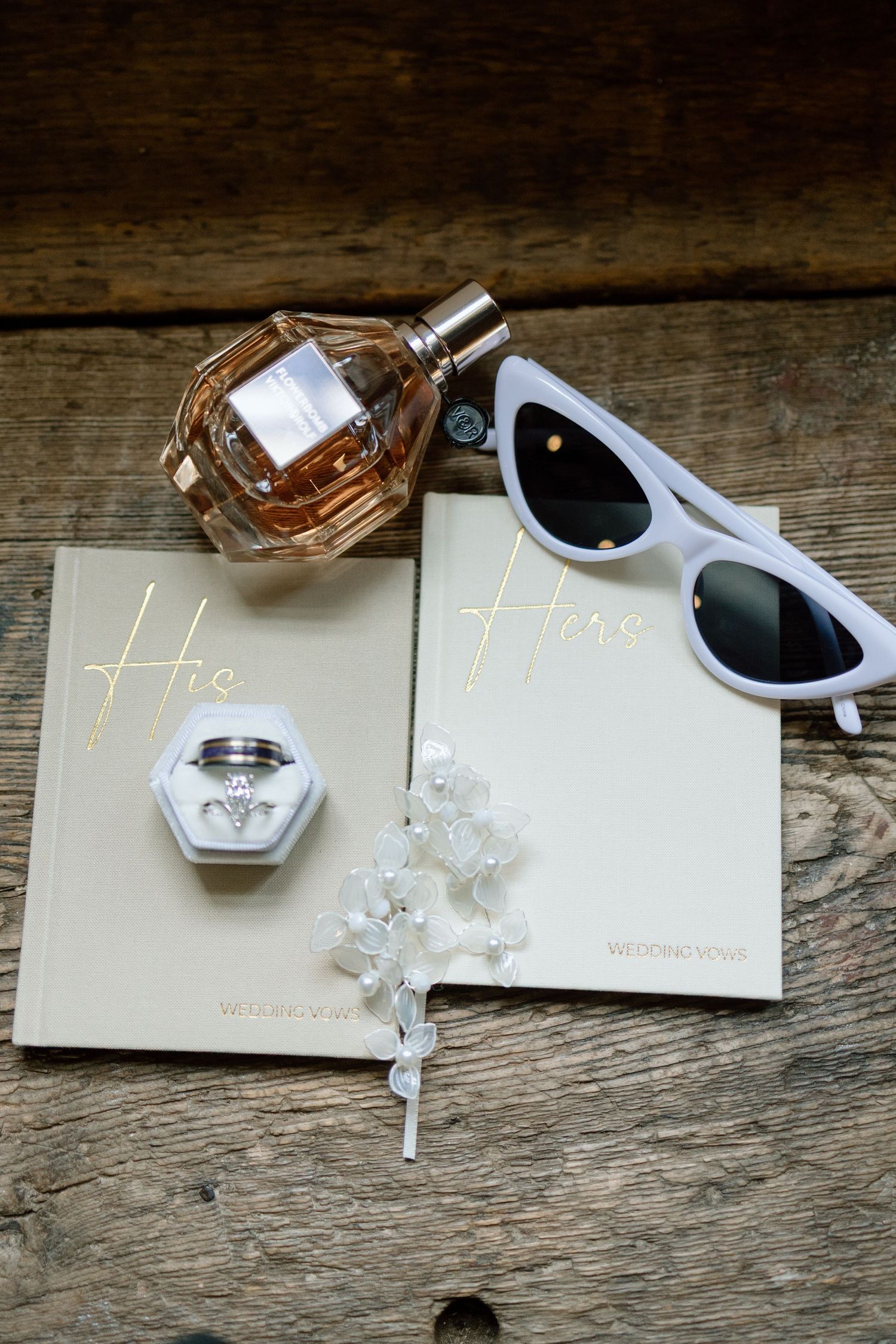 White sunglasses and a small glass perfume bottle arranged on rustic wooden surface with delicate decorative elements.