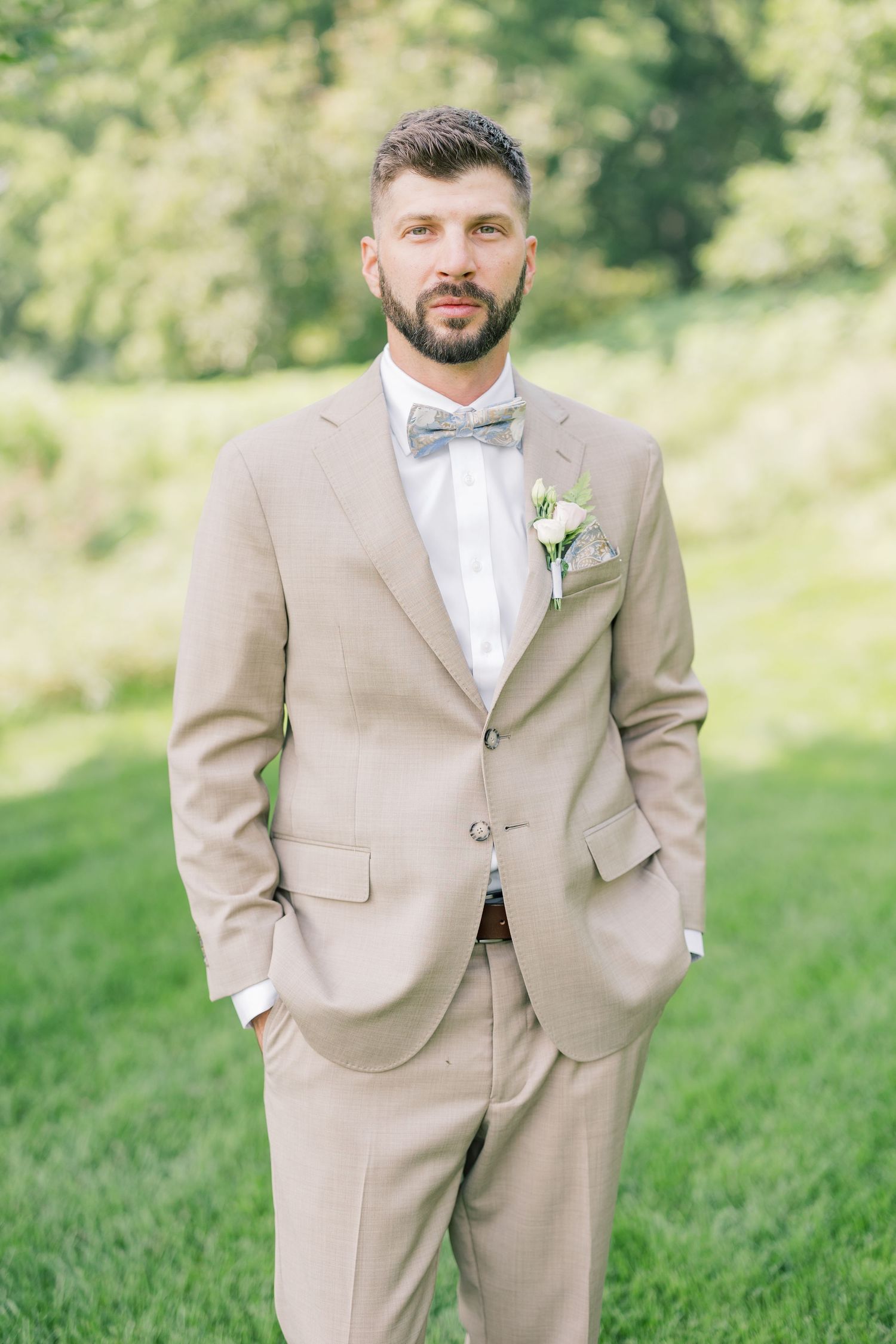 Groomsmen in beige suits and bow ties stand in a garden setting.