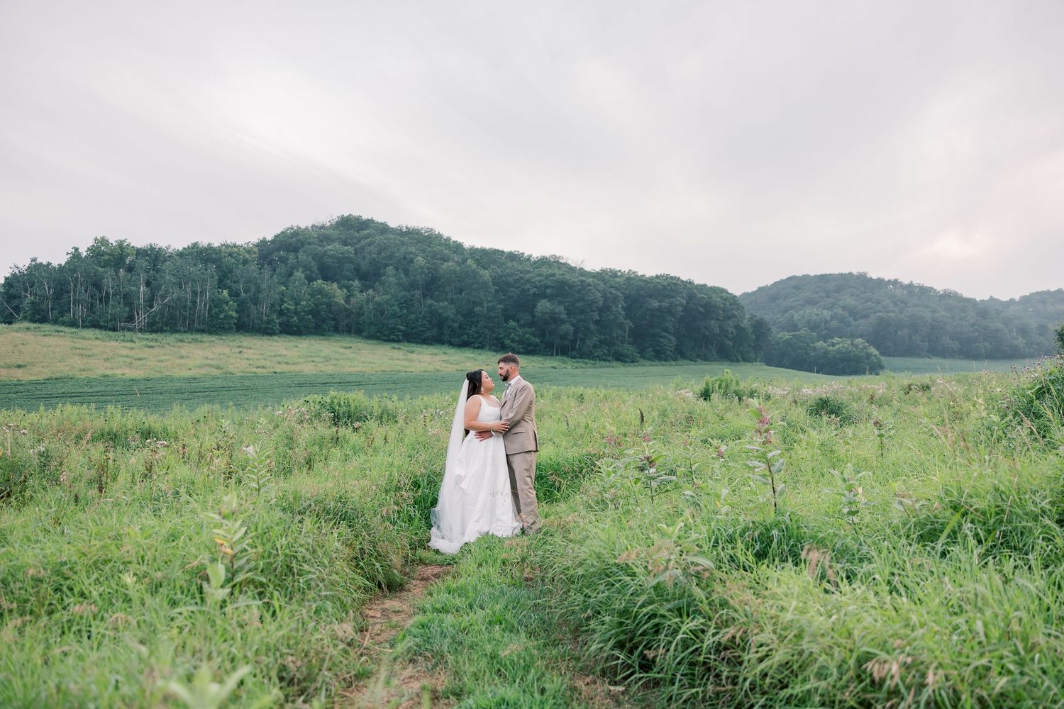 A wedding couple stands together in a misty mountain meadow.
