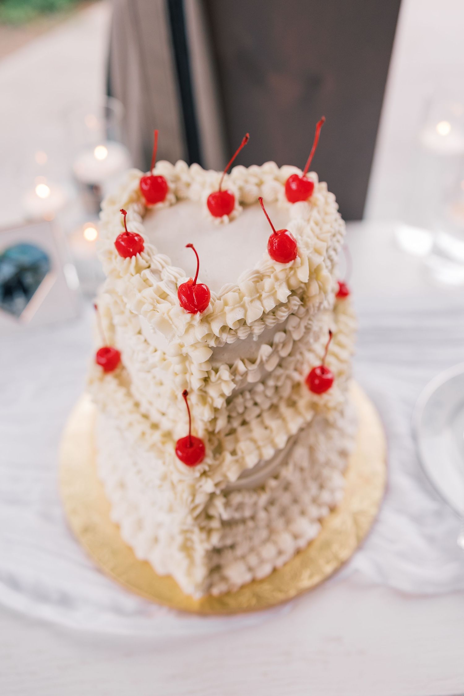 White wedding cake decorated with delicate frosting and topped with bright red maraschino cherries.