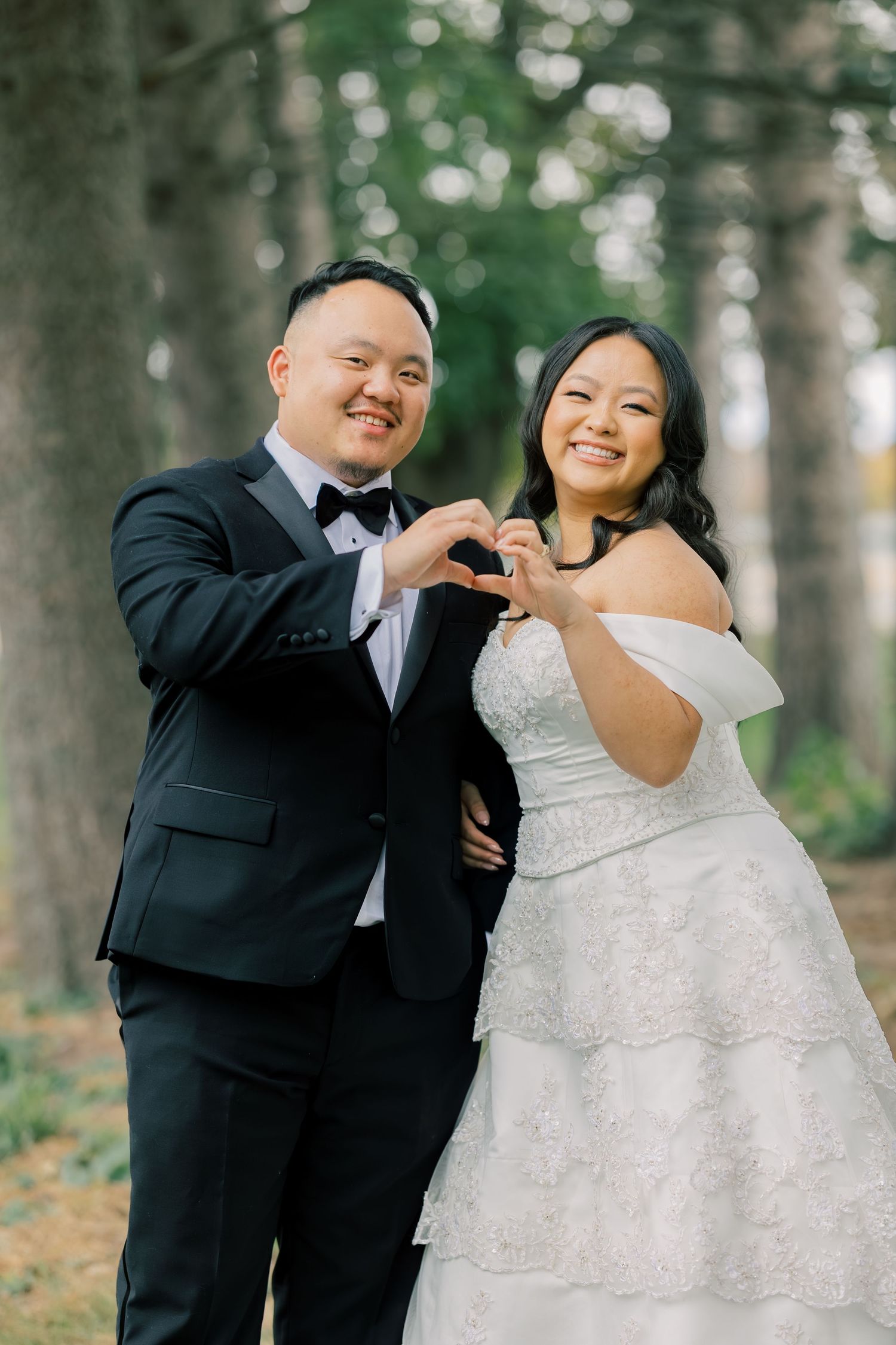 A couple shares joyful moments and playful dance moves in a wooded outdoor setting.