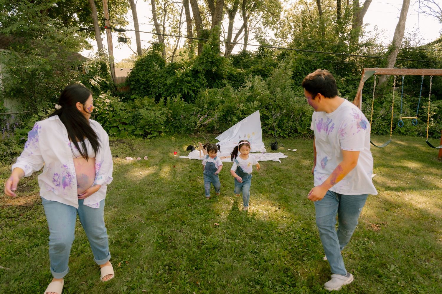 Family playing in backyard with kite on green grass, surrounded by trees and swing set.