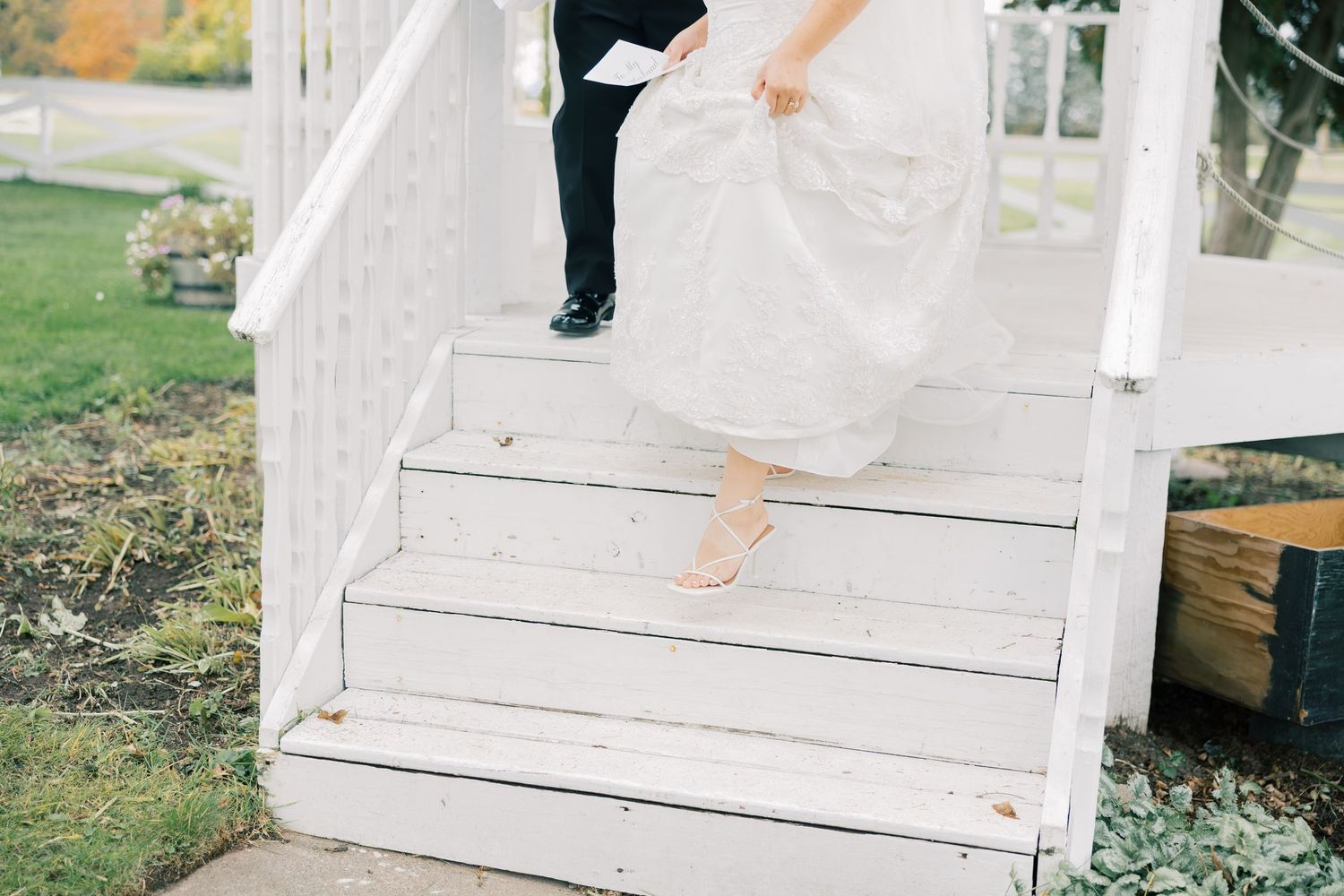 A close-up view of white wedding dress details and shoes on light stone steps during an outdoor ceremony.