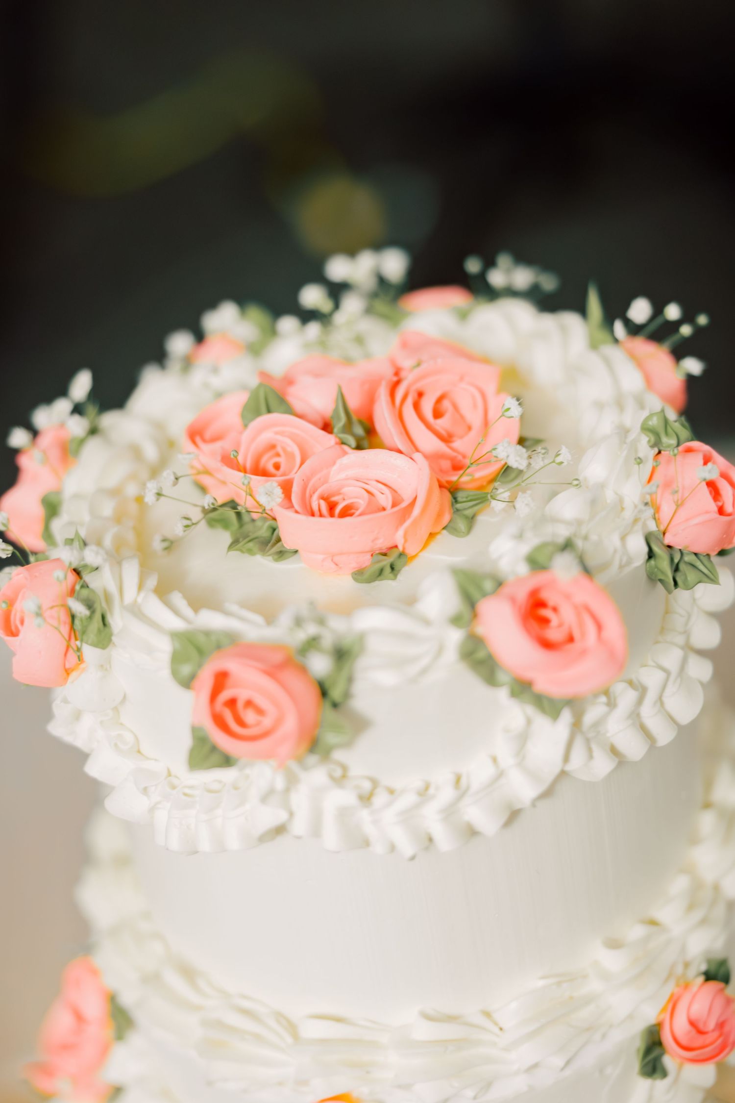 A white wedding cake decorated with delicate coral roses and white lily of the valley flowers on top.