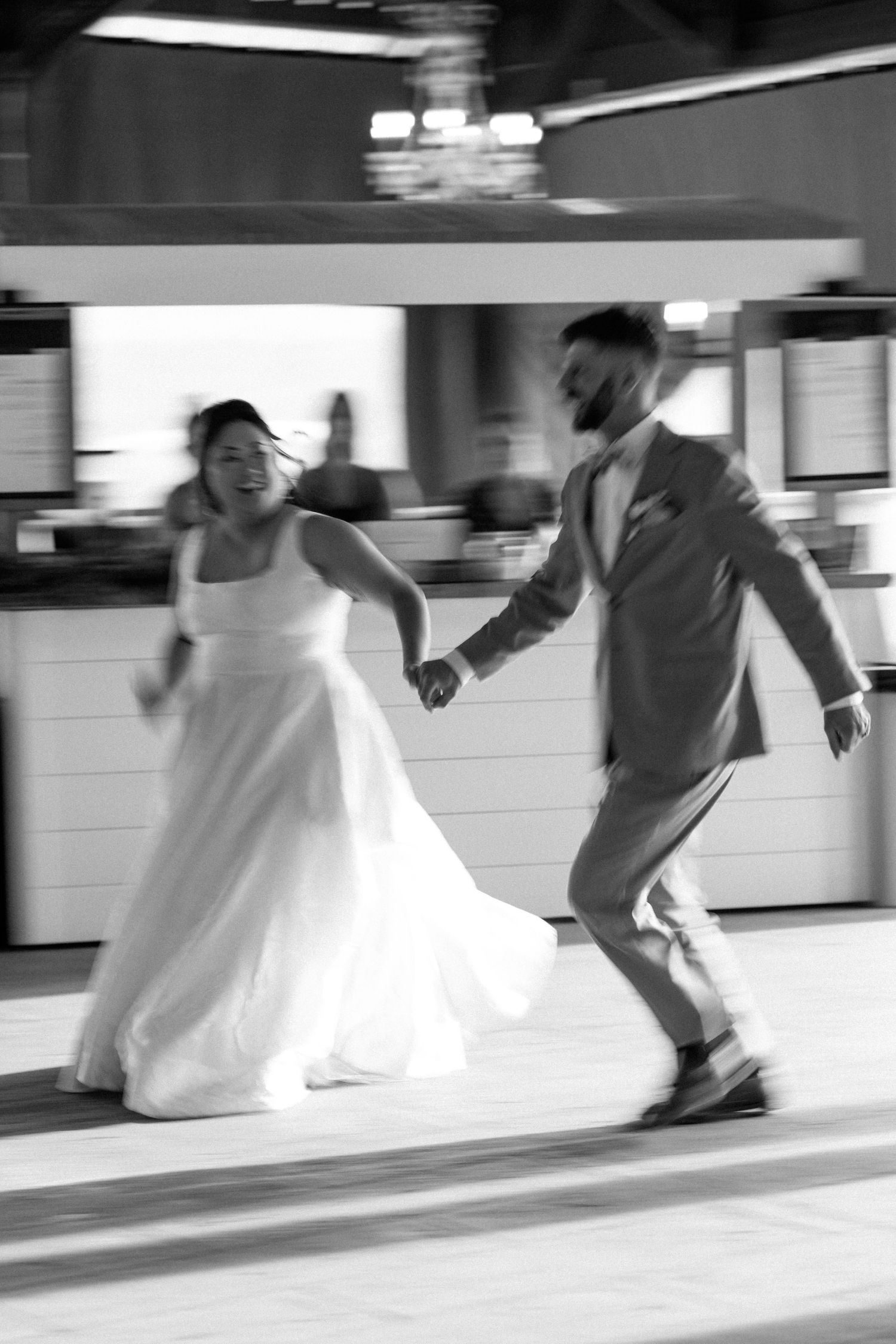 Motion-blurred black and white photo of people dancing at a wedding reception.