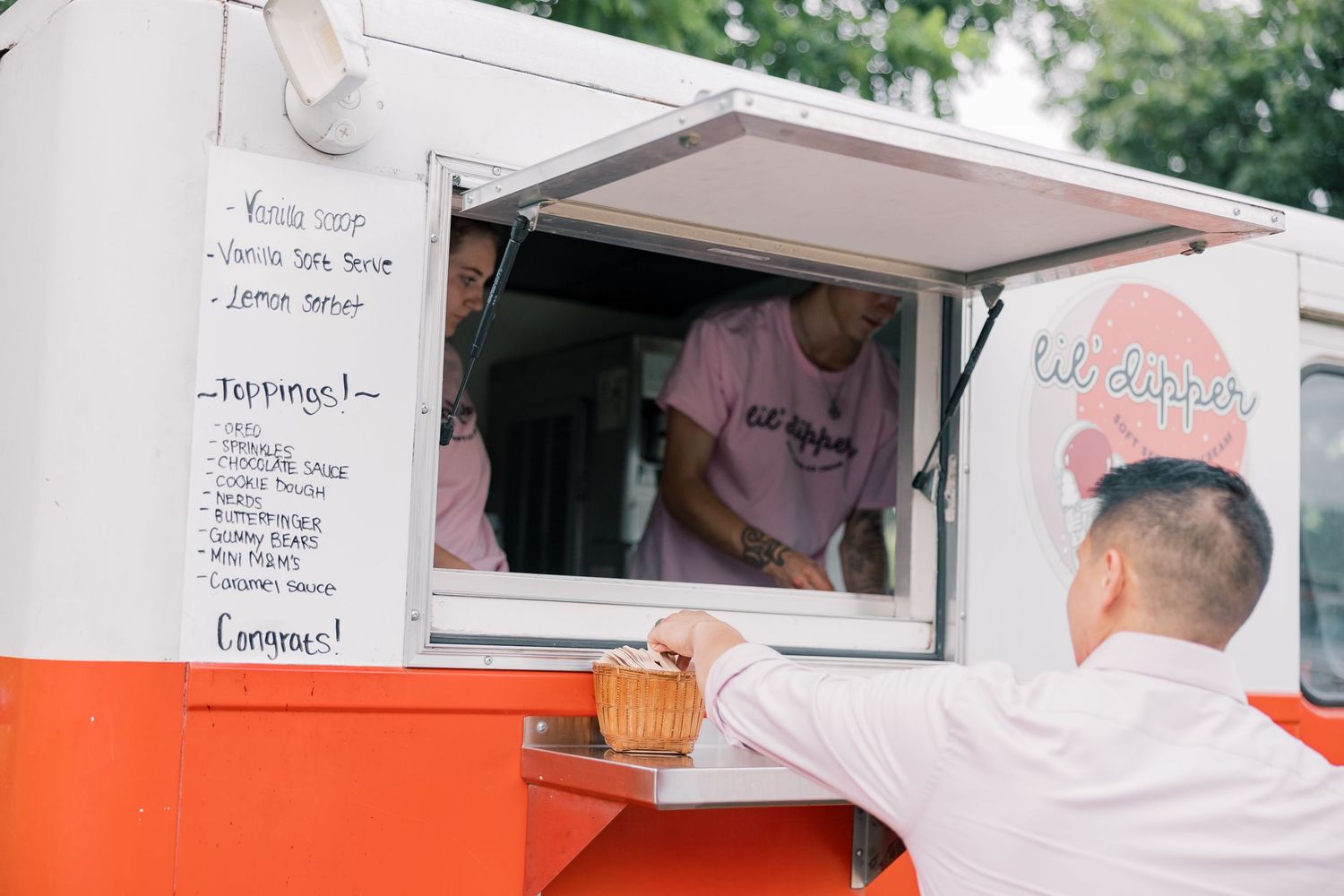 An orange food truck window with a menu board and staff member serving guests.