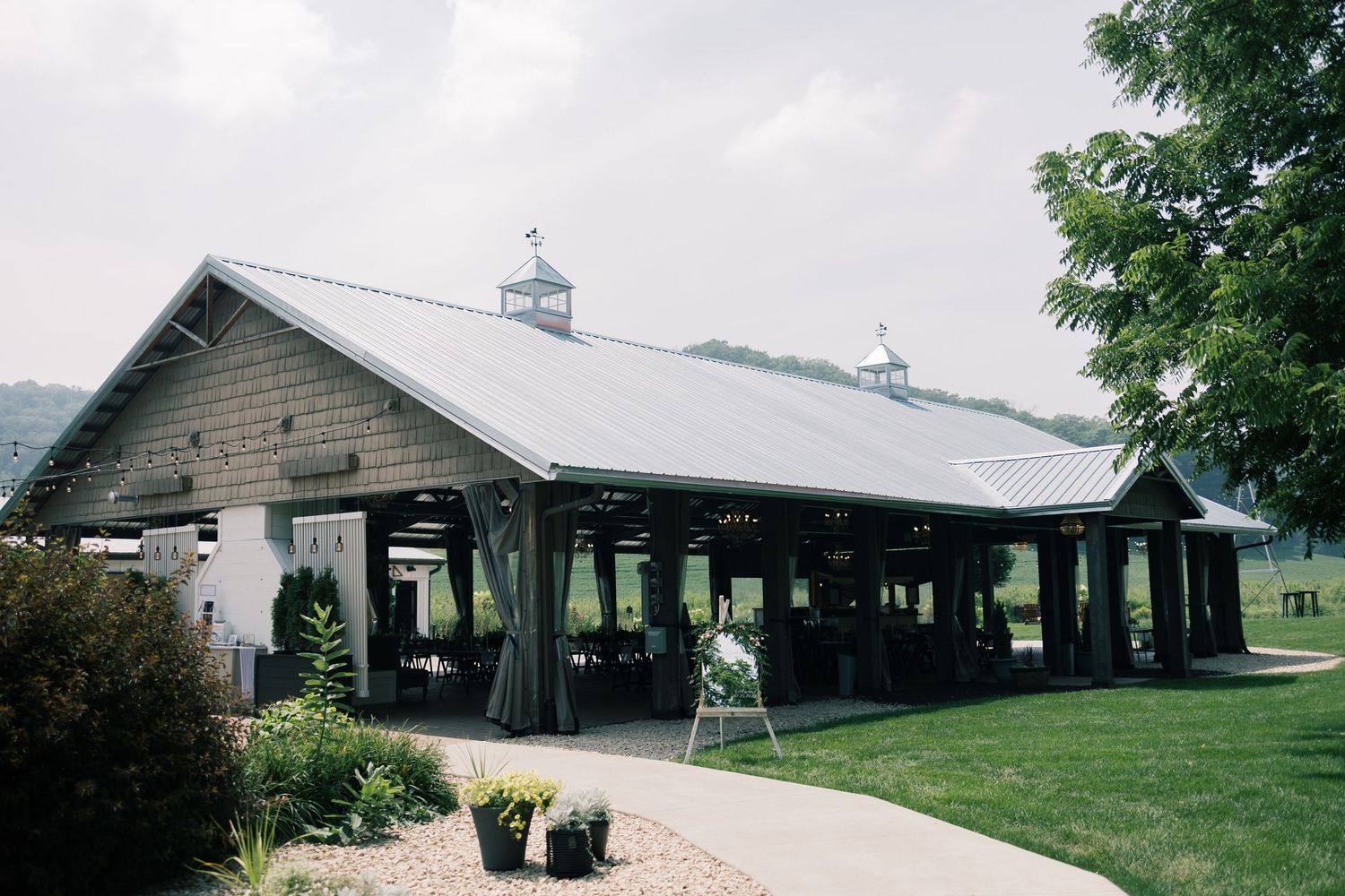 A covered outdoor pavilion venue with green lawn and landscaping under cloudy skies.