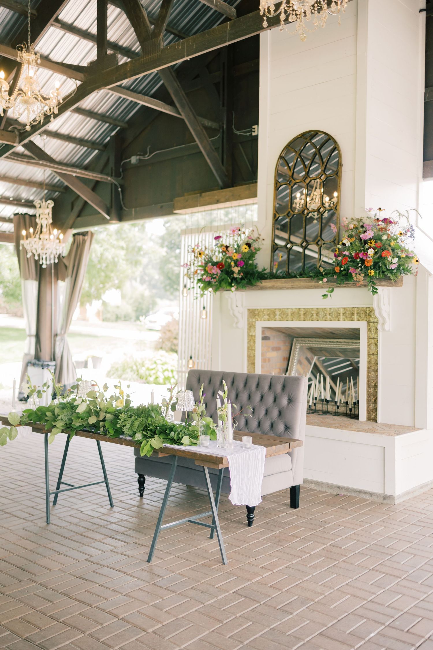 Elegant wedding venue with crystal chandeliers, floral arrangements, and a fireplace with grey tufted seating.