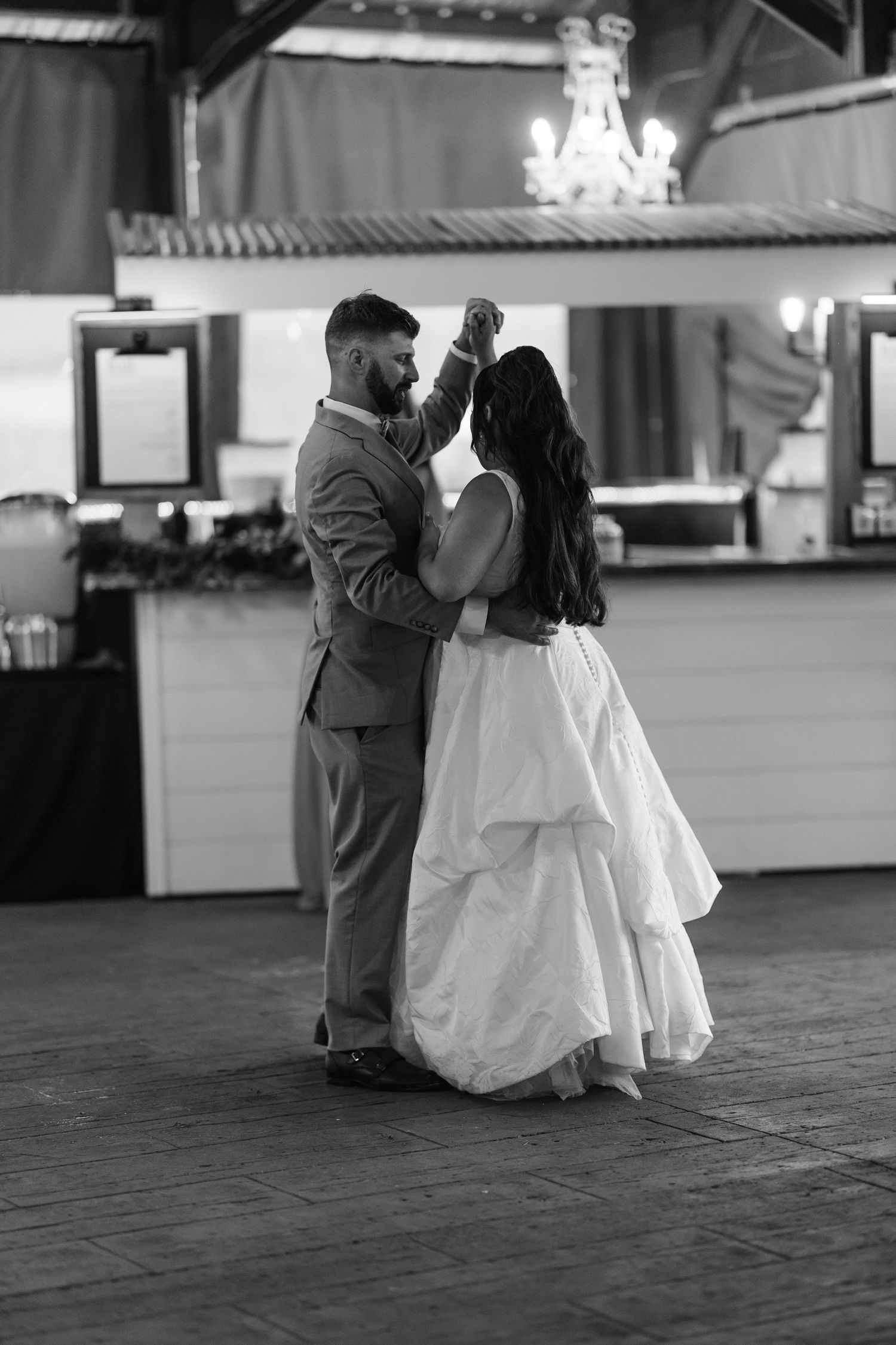 A couple shares their first dance at a wedding reception in black and white photography on a wooden dance floor.