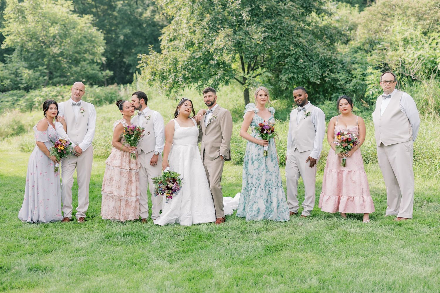 Wedding party in soft pastels and gray poses together on a grassy hillside.