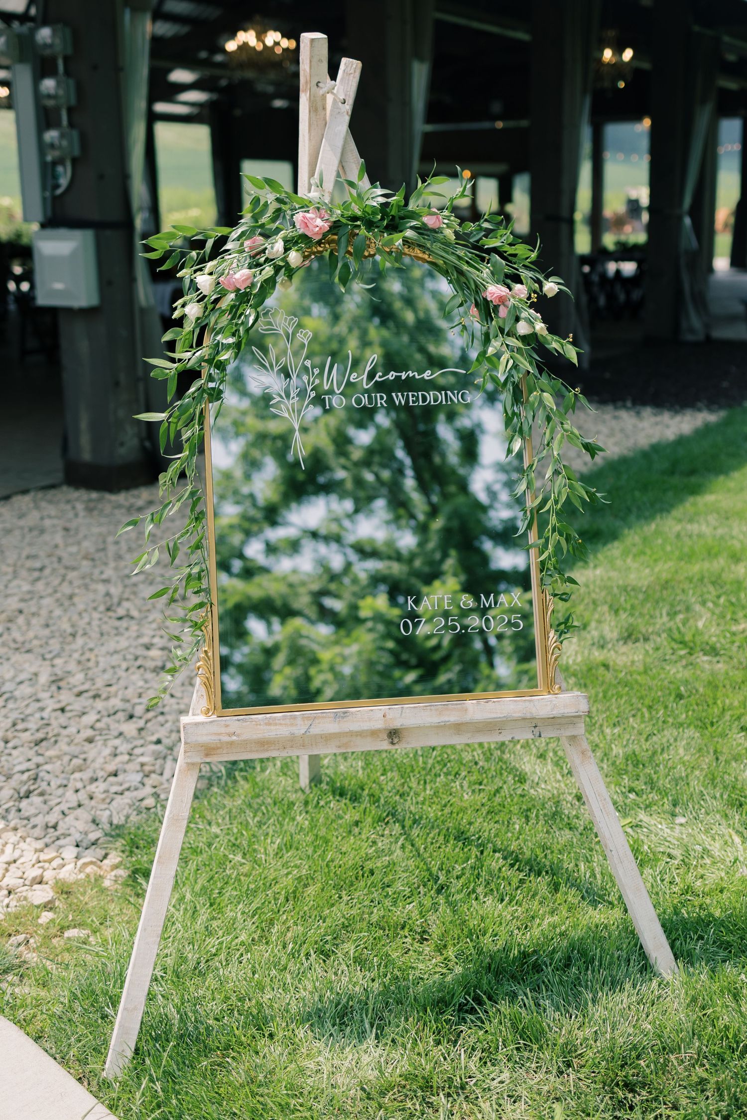 Wooden easels with decorative floral arrangements stand on a grassy lawn at an outdoor wedding venue.