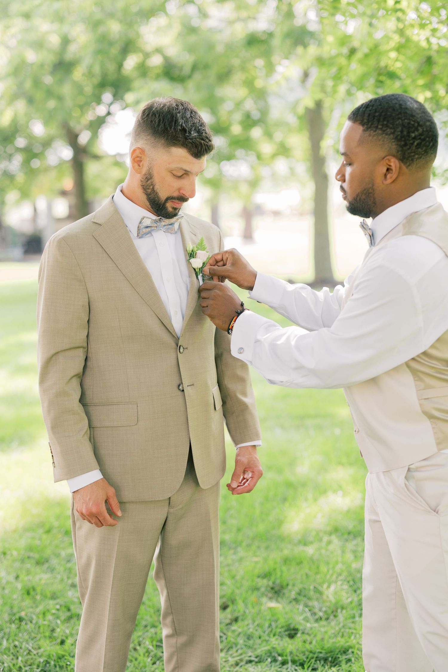 Two groomsmen in coordinating formal suits interact candidly during an outdoor photo session.
