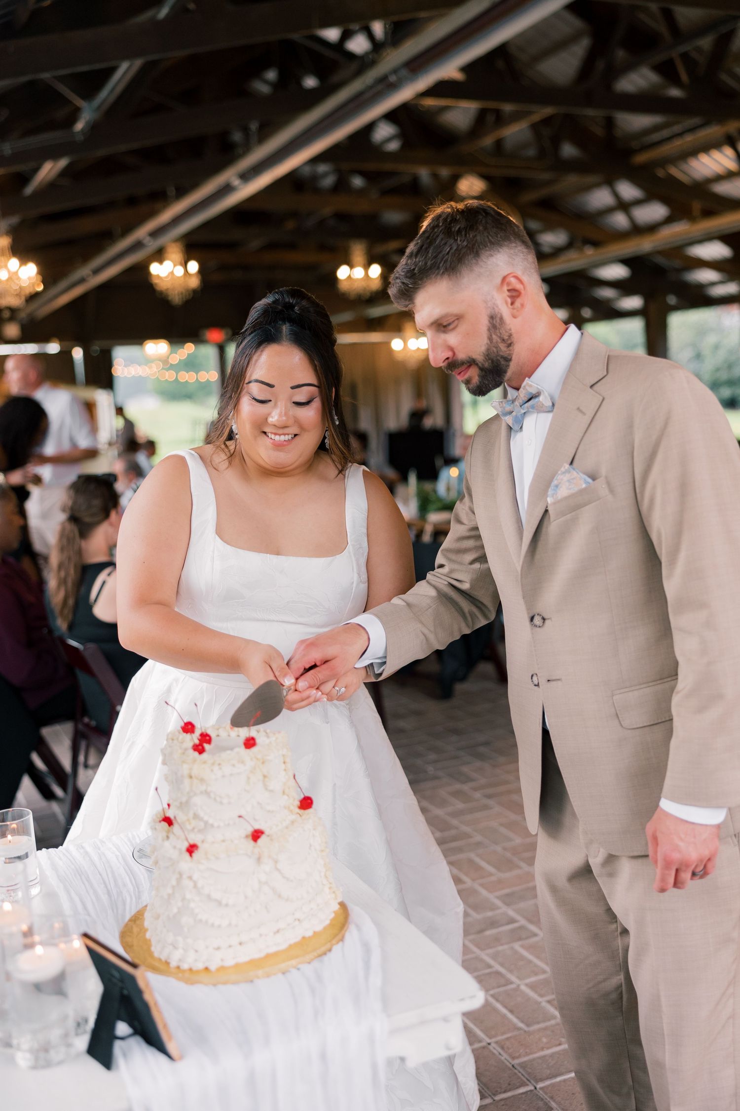Wedding couple cuts their white and red decorated cake together at a rustic venue reception.