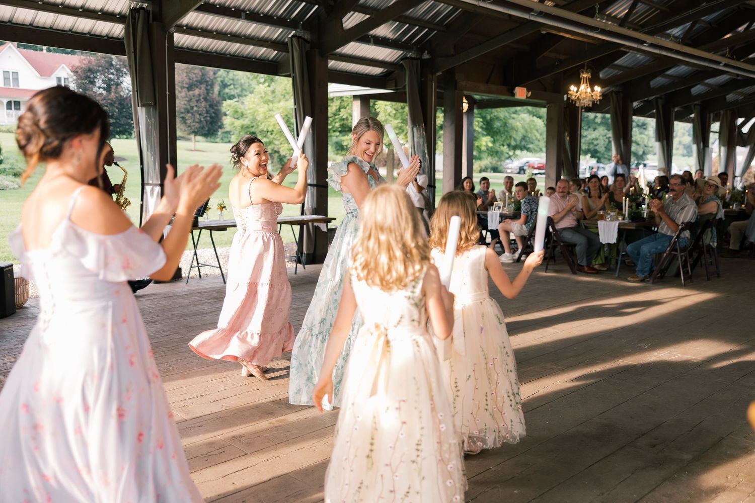 Wedding celebration with dancing in a rustic covered venue with streaming sunlight.