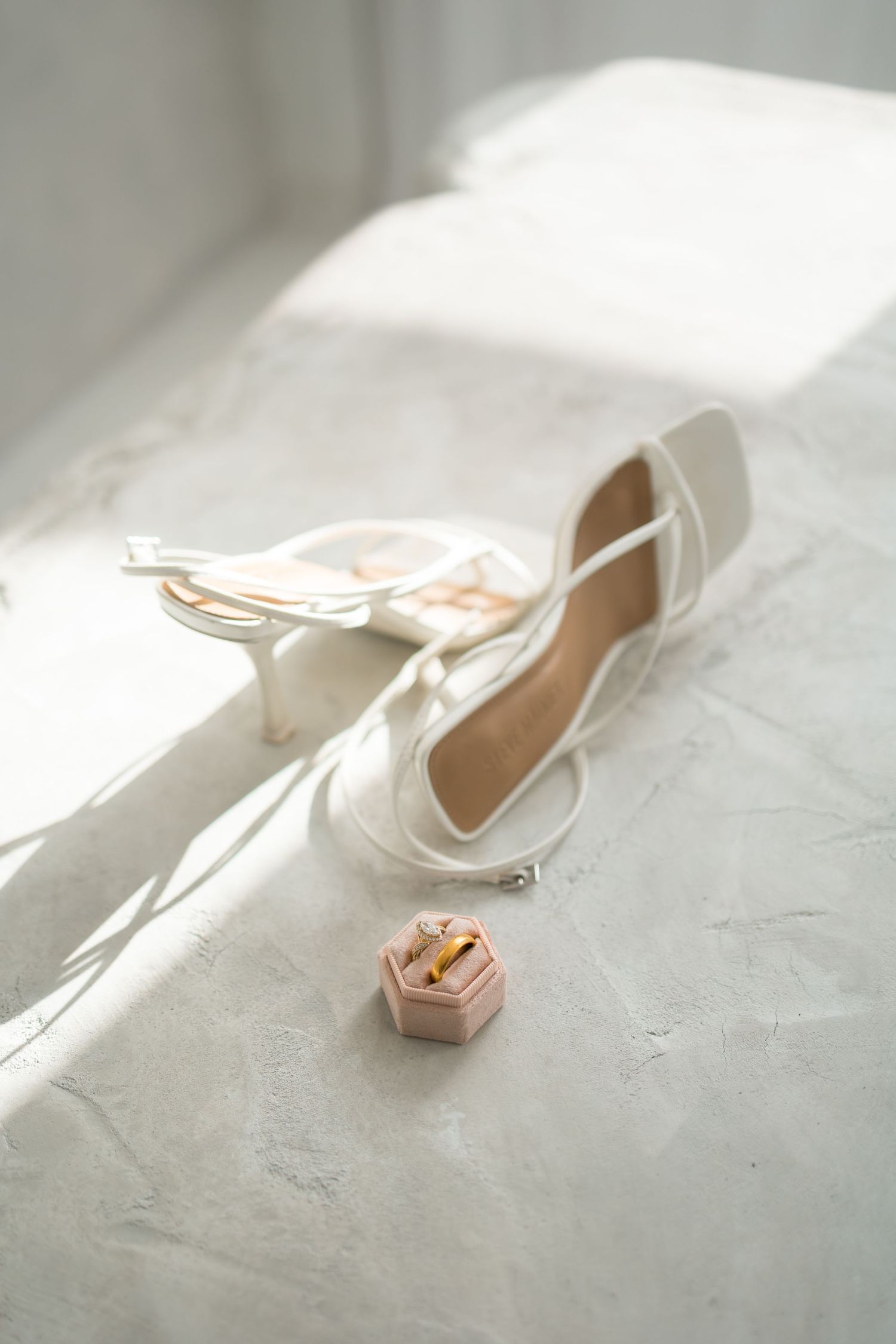 Elegant white wedding shoes with delicate details photographed in soft natural light on a textured surface.