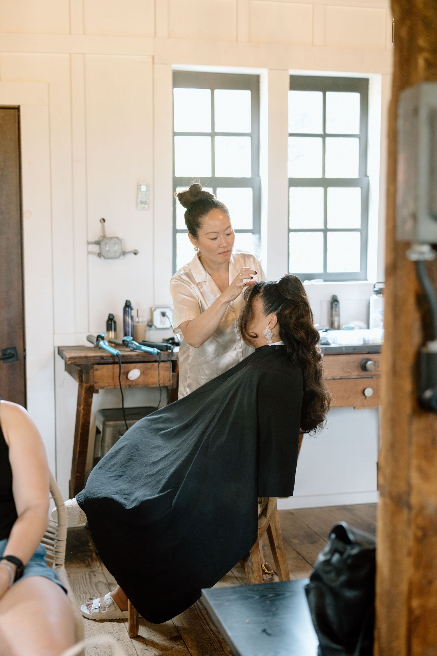 A hairdressing scene showing someone working on a client's hair in a bright interior setting.