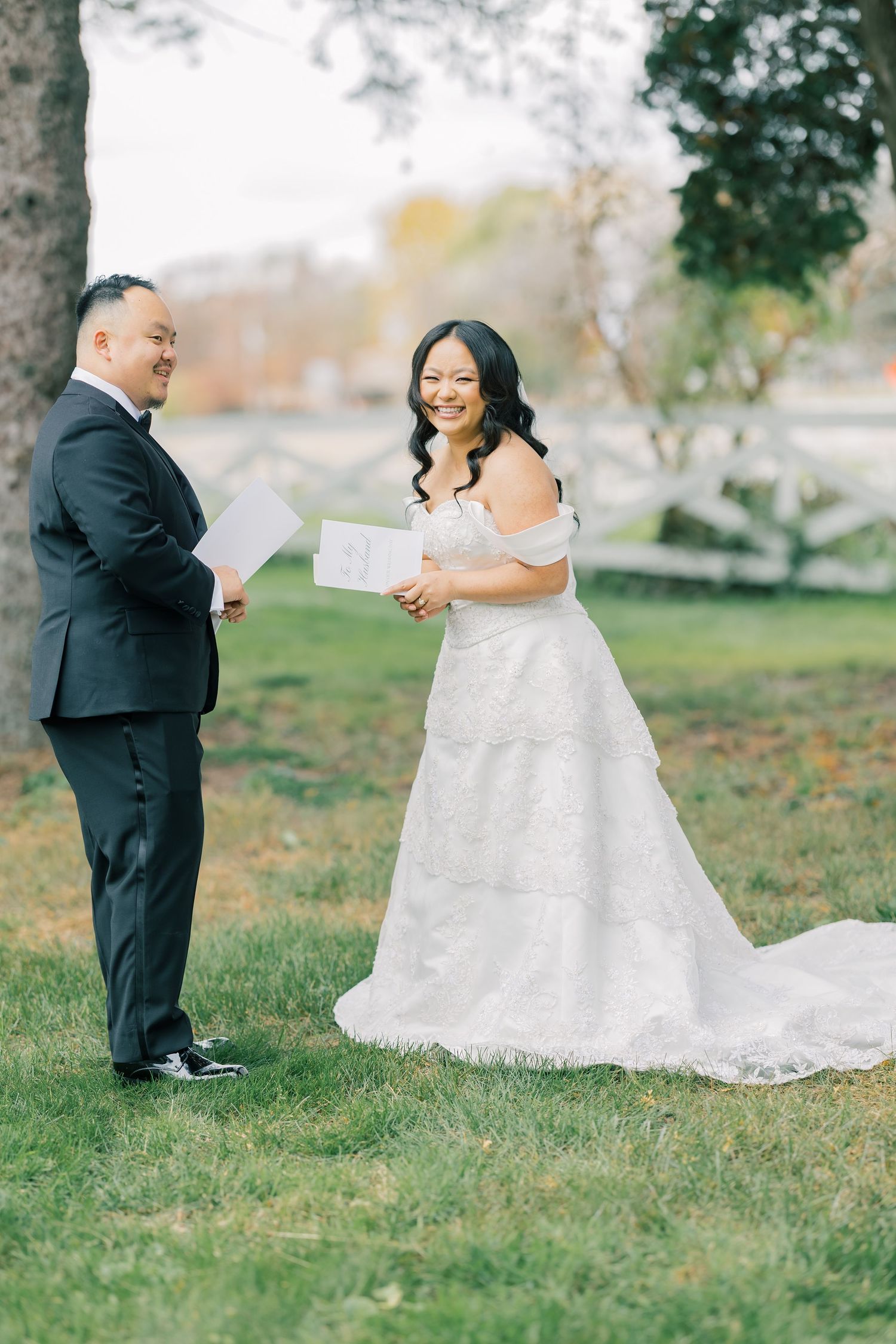 Newlyweds read personal vows to each other surrounded by trees in an intimate outdoor ceremony setting.