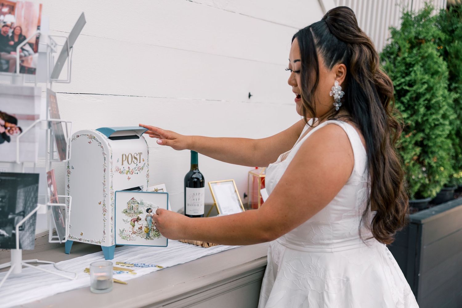 A bride in a white dress interacts with a vintage-style mailbox at a wedding reception.