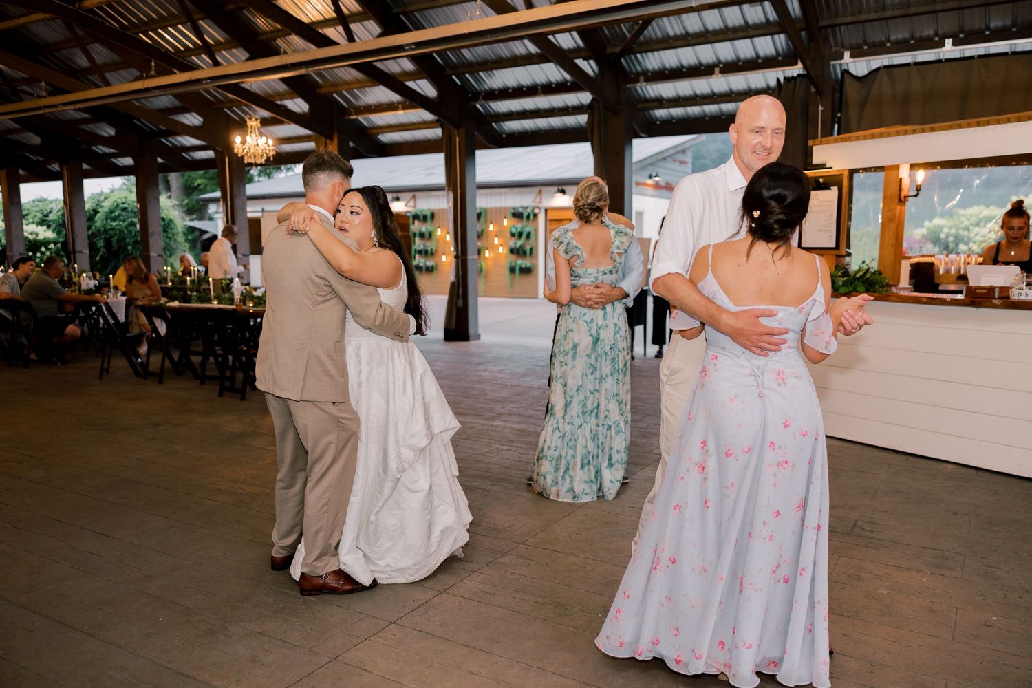 Wedding reception guests dancing and celebrating in a rustic covered venue space.
