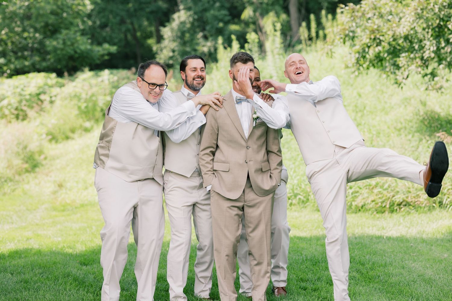 Wedding party in light beige suits celebrating outdoors.