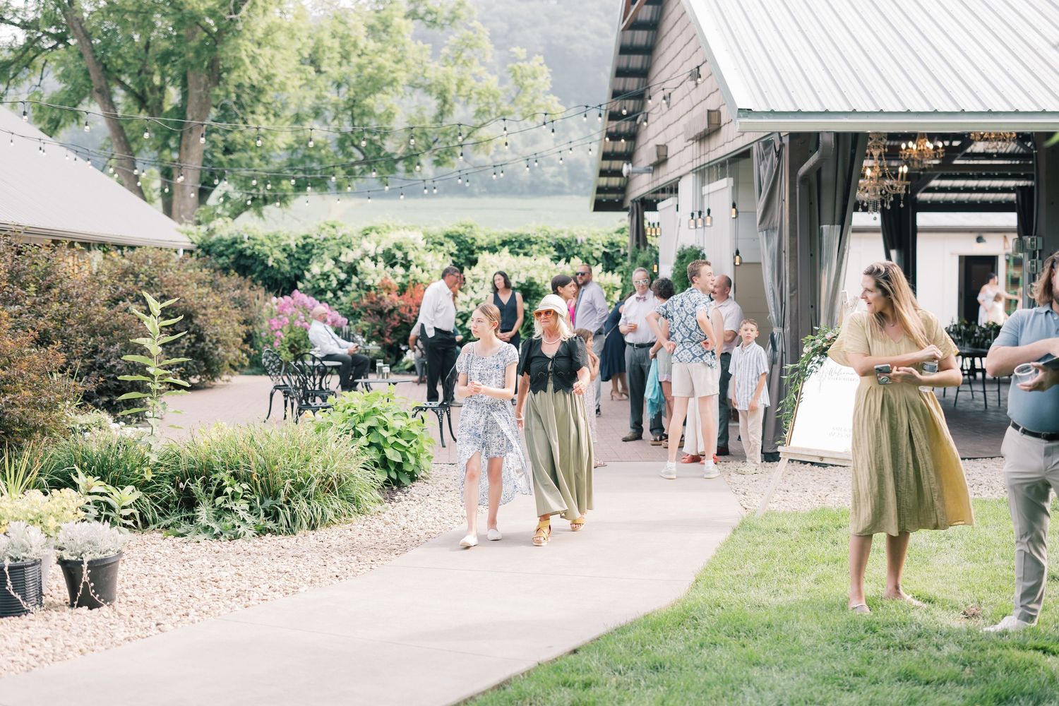 Wedding guests mingling outside a rustic venue surrounded by beautiful landscaping.