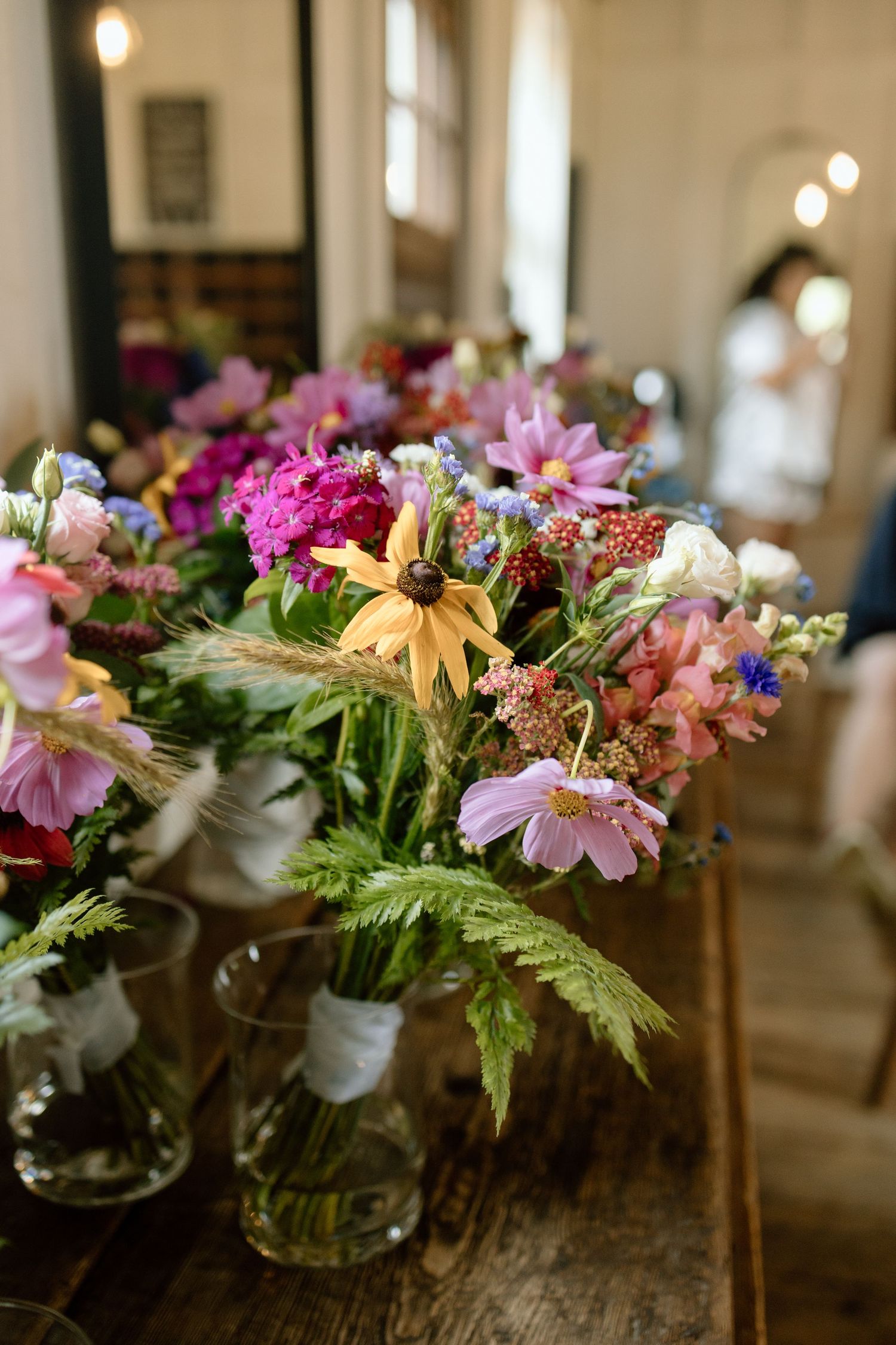 Colorful wildflower arrangements in mason jars displayed on a rustic wooden table with soft lighting.