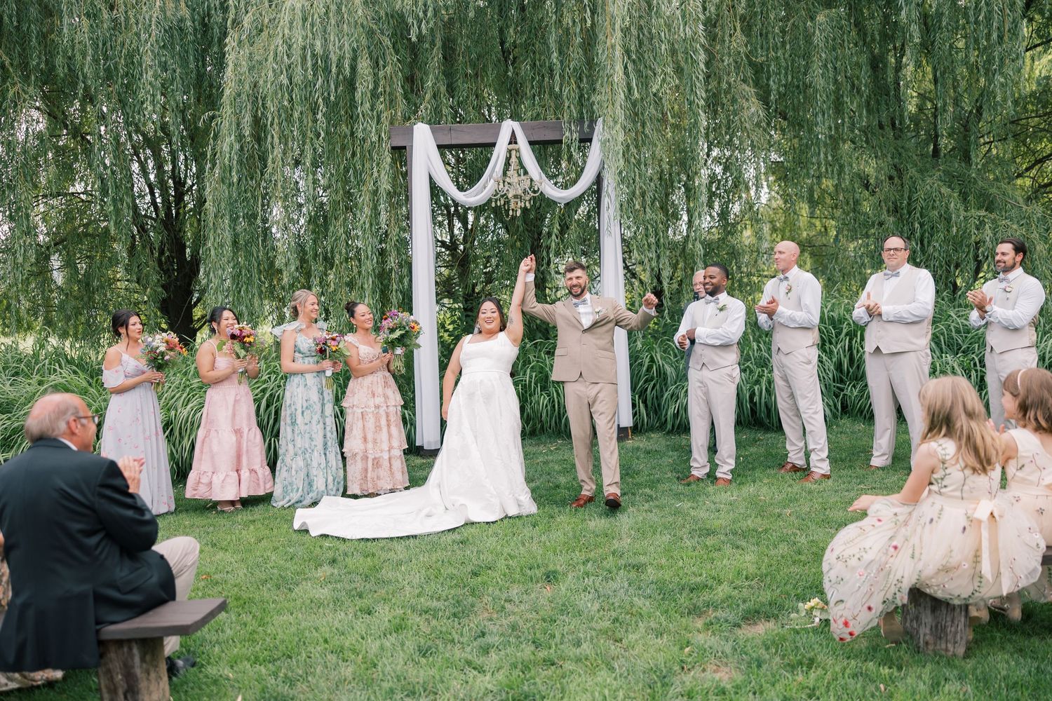 Wedding party gathered outdoors in a wooded setting with natural greenery backdrop.