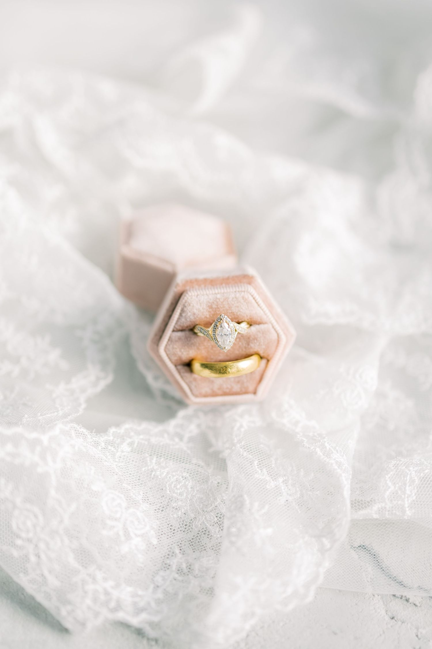 Pink hexagonal ring box containing wedding rings displayed on white lace fabric.